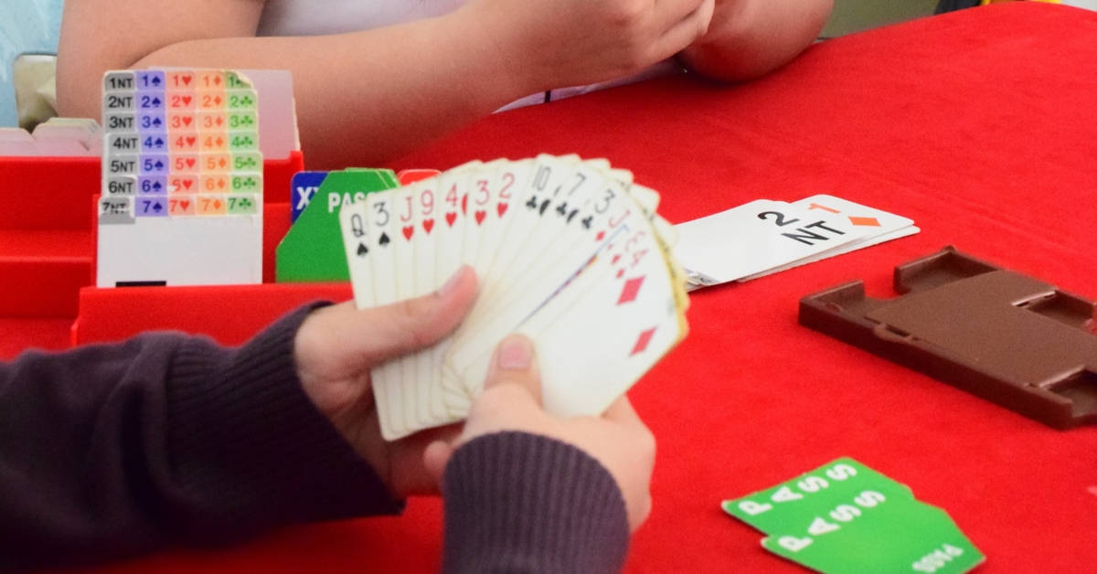 game 桌布 壁紙 — 特寫鏡頭，雙手在紅色桌子上扇動橋牌撲克牌，旁邊有叫牌盒和已過的牌。