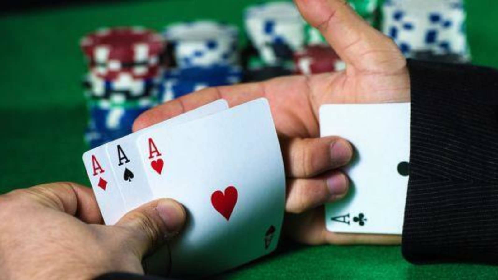 Poker 桌布 壁紙 — 特寫鏡頭，雙手在綠色賭桌上持有三張A，背景有色彩繽紛的籌碼堆。