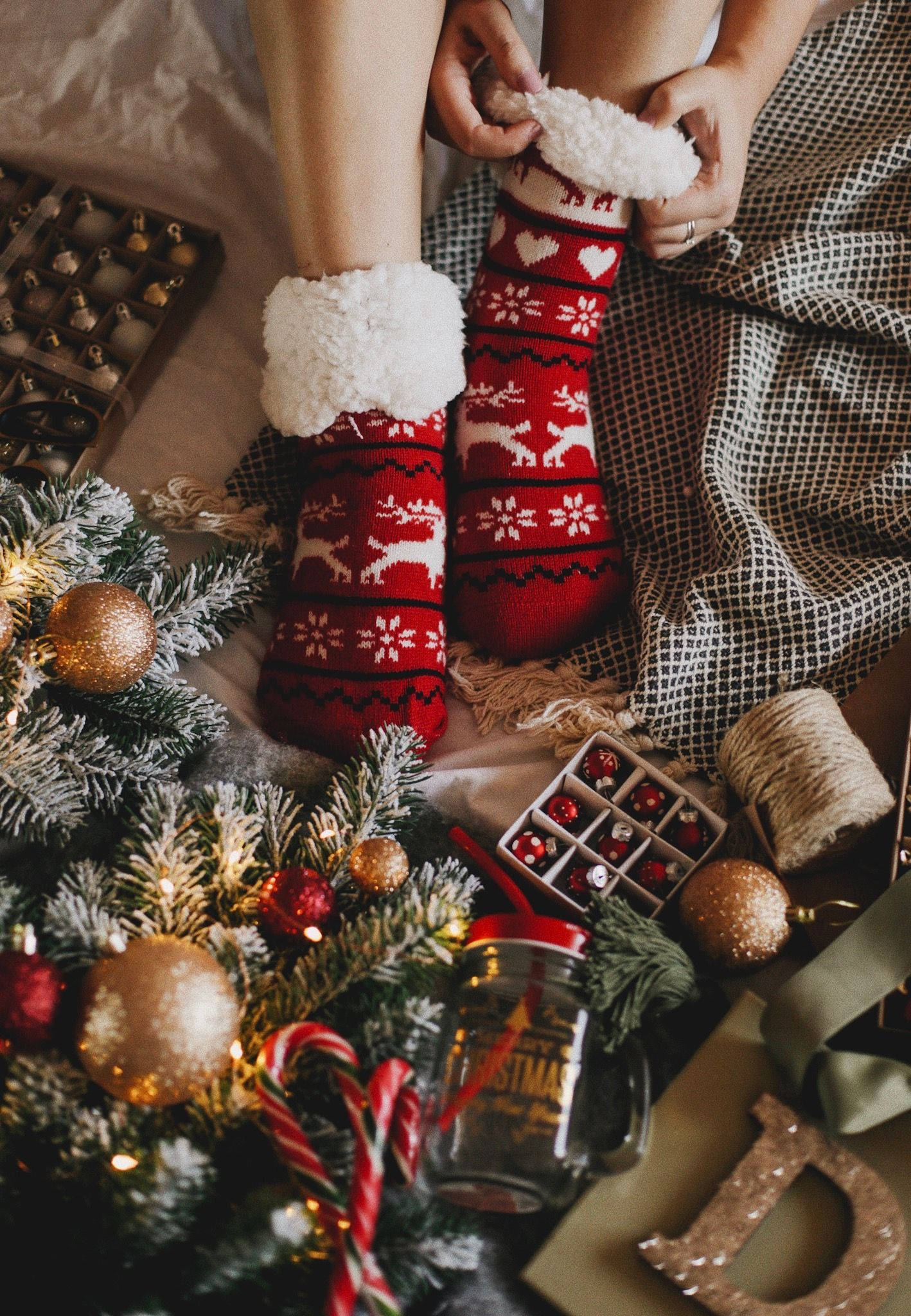 Cozy 桌布 壁紙 — 特寫鏡頭：雙手在裝飾好的聖誕樹和飾品旁穿上節日紅色馴鹿圖案襪子。