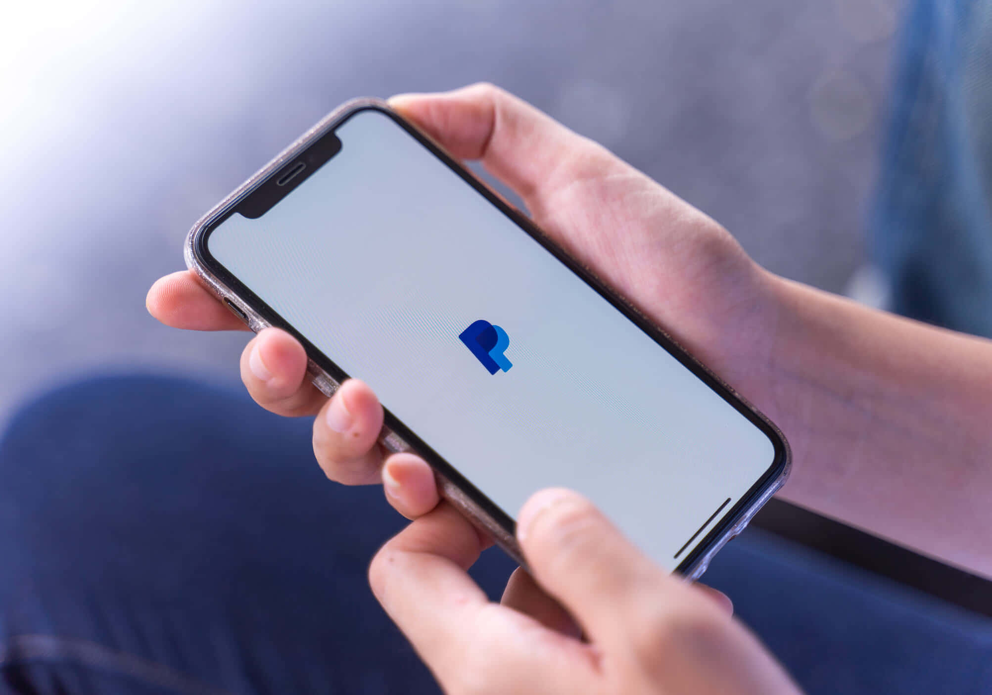 PayPal 桌布 壁紙 — 特寫鏡頭，雙手拿著一部智慧型手機，螢幕上顯示PayPal標誌。