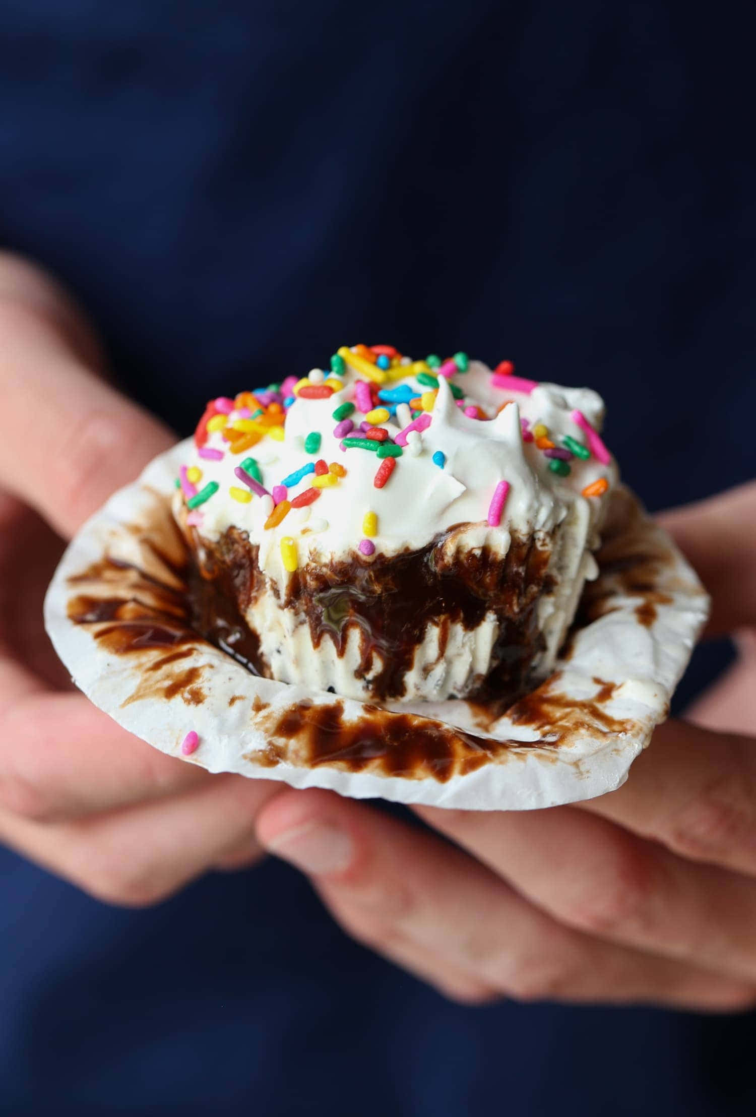 Cupcake 桌布 壁紙 — 特寫鏡頭，雙手捧著一個淋上巧克力醬的冰淇淋紙杯蛋糕，上面綴滿彩色糖針和鮮奶油。