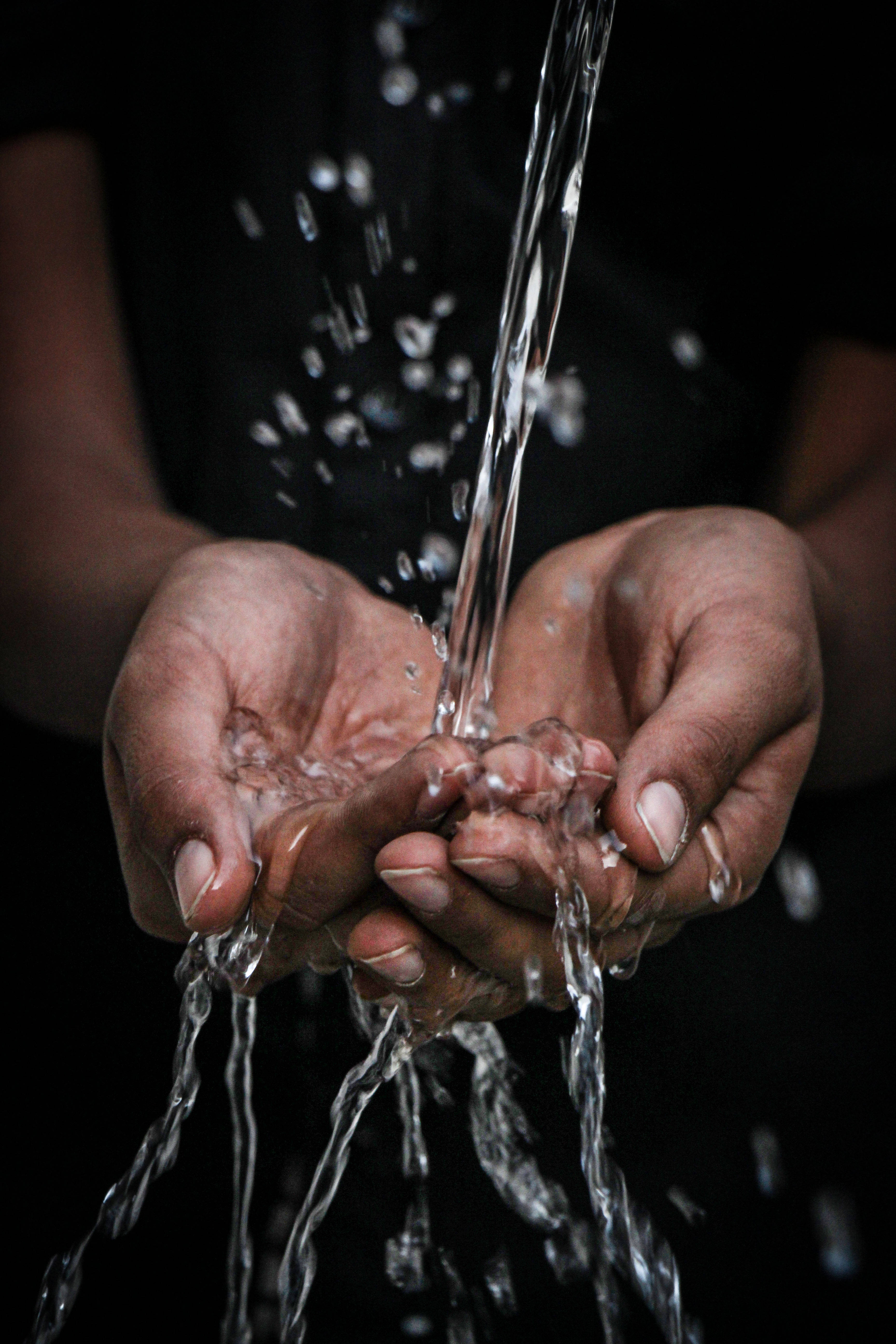 Drink Water 桌布 壁紙 — 特寫鏡頭，雙手捧著清澈的水流，背景為黑色，水滴在空中懸浮移動。