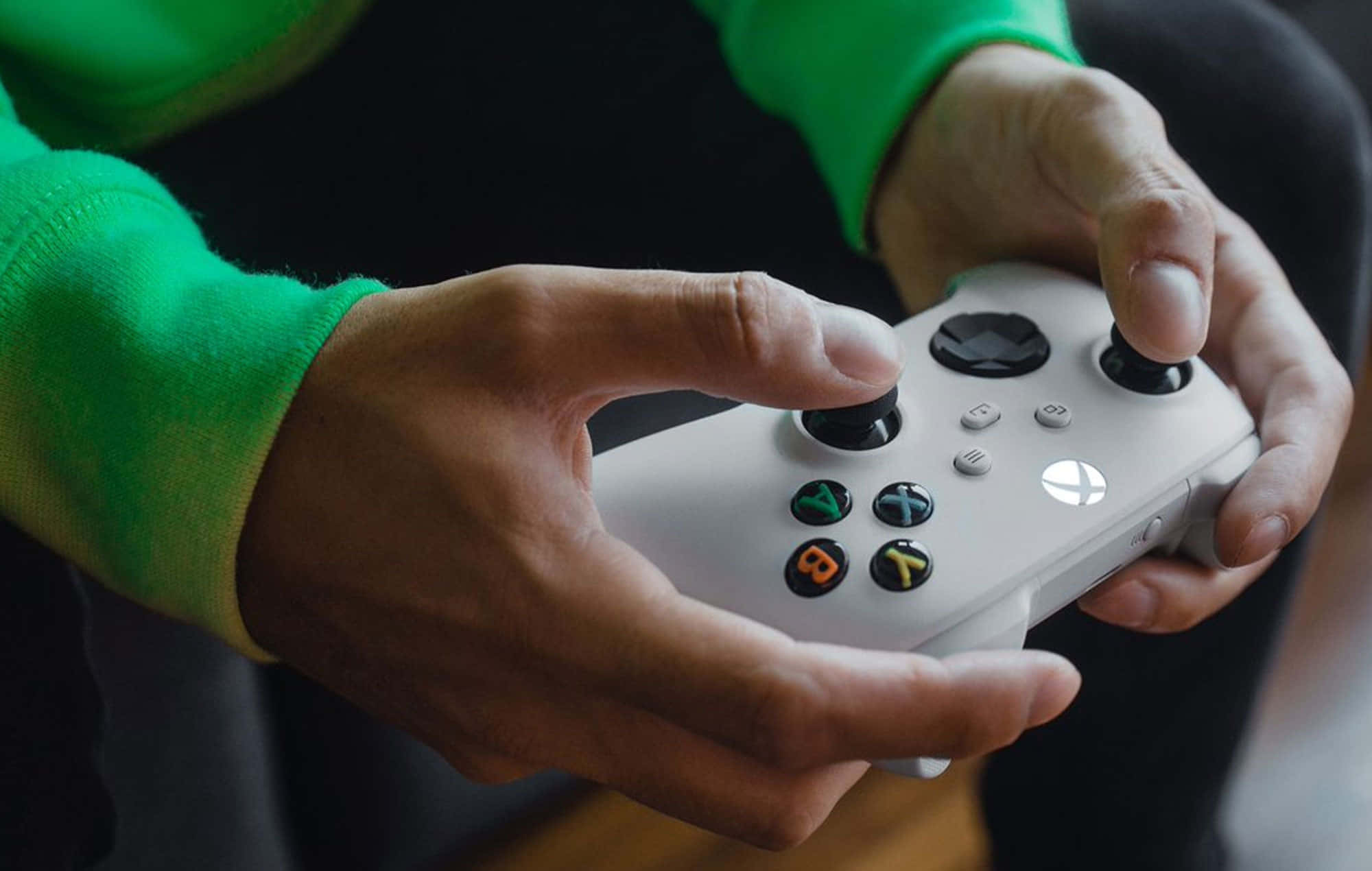 Xbox 360 Gamer 桌布 壁紙 — 特寫鏡頭，雙手緊握白色Xbox控制器，綠色保護套在深色背景下清晰可見。