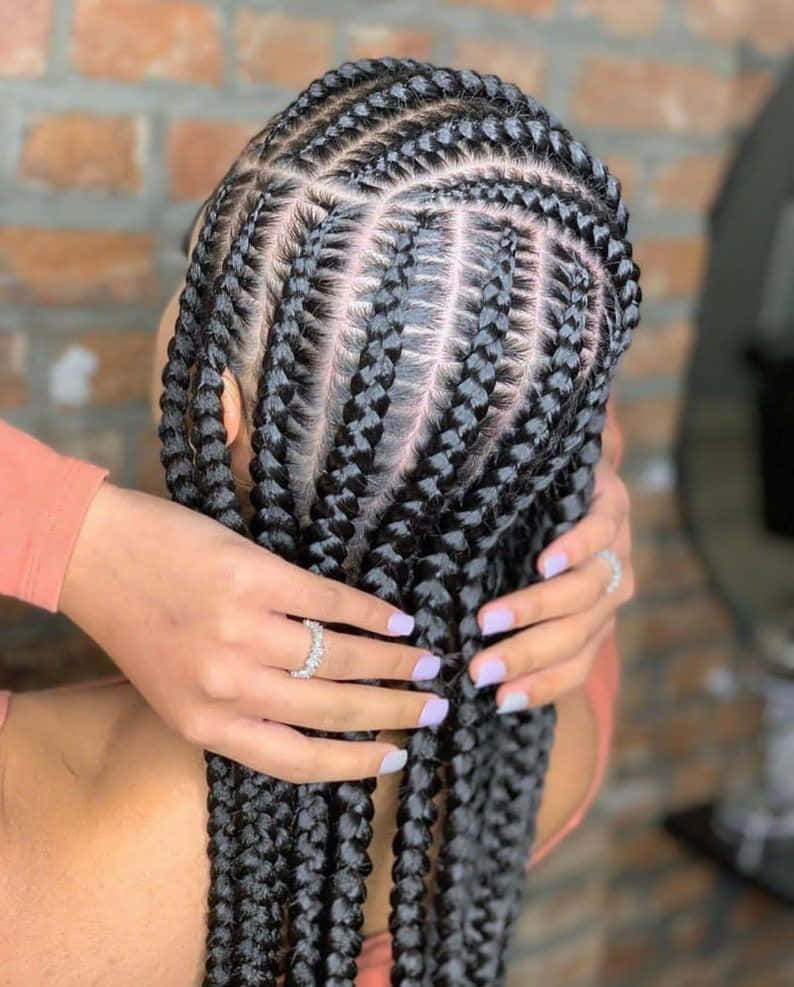 Cute Hairstyles 桌布 壁紙 — 特寫鏡頭，雙手輕柔地握著複雜的箱形辮子，背景是磚牆。