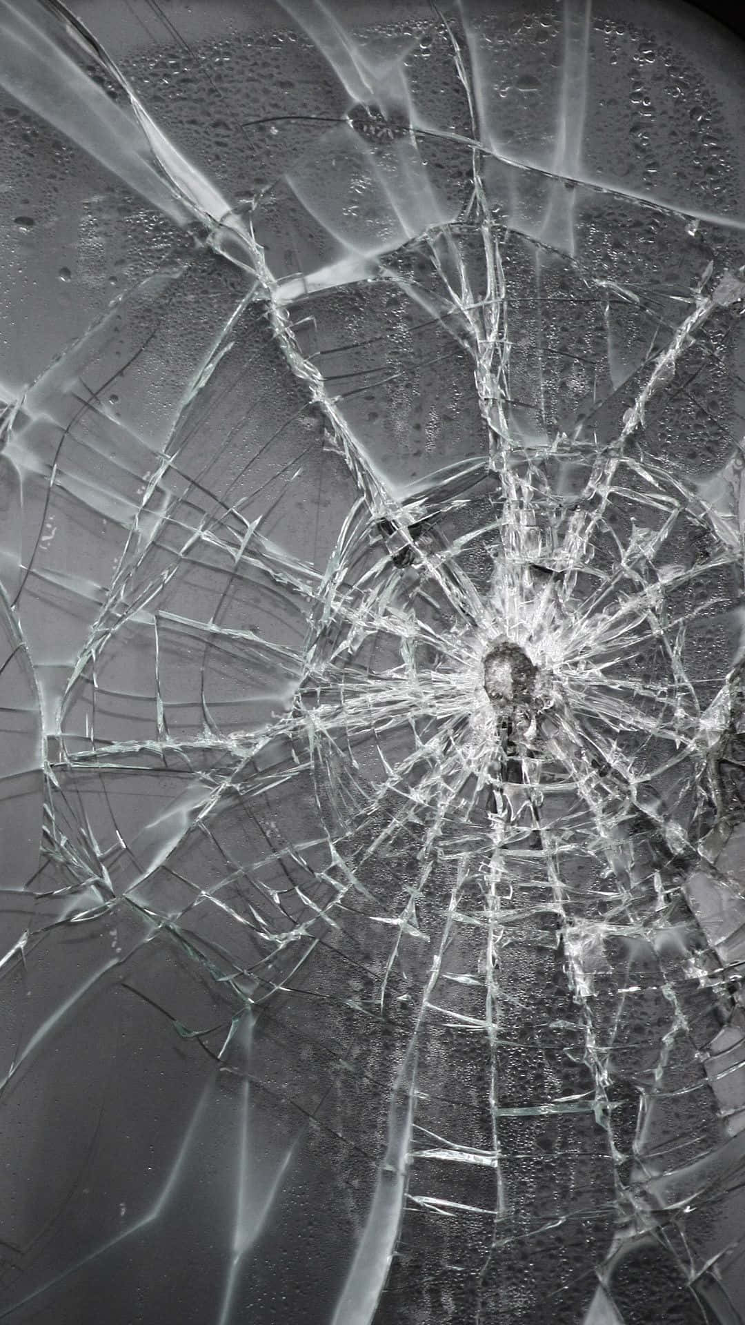 桌布 壁紙 — 特寫鏡頭，顯示一塊破碎玻璃，從中央撞擊點向外輻射出複雜裂紋，背景為深色。