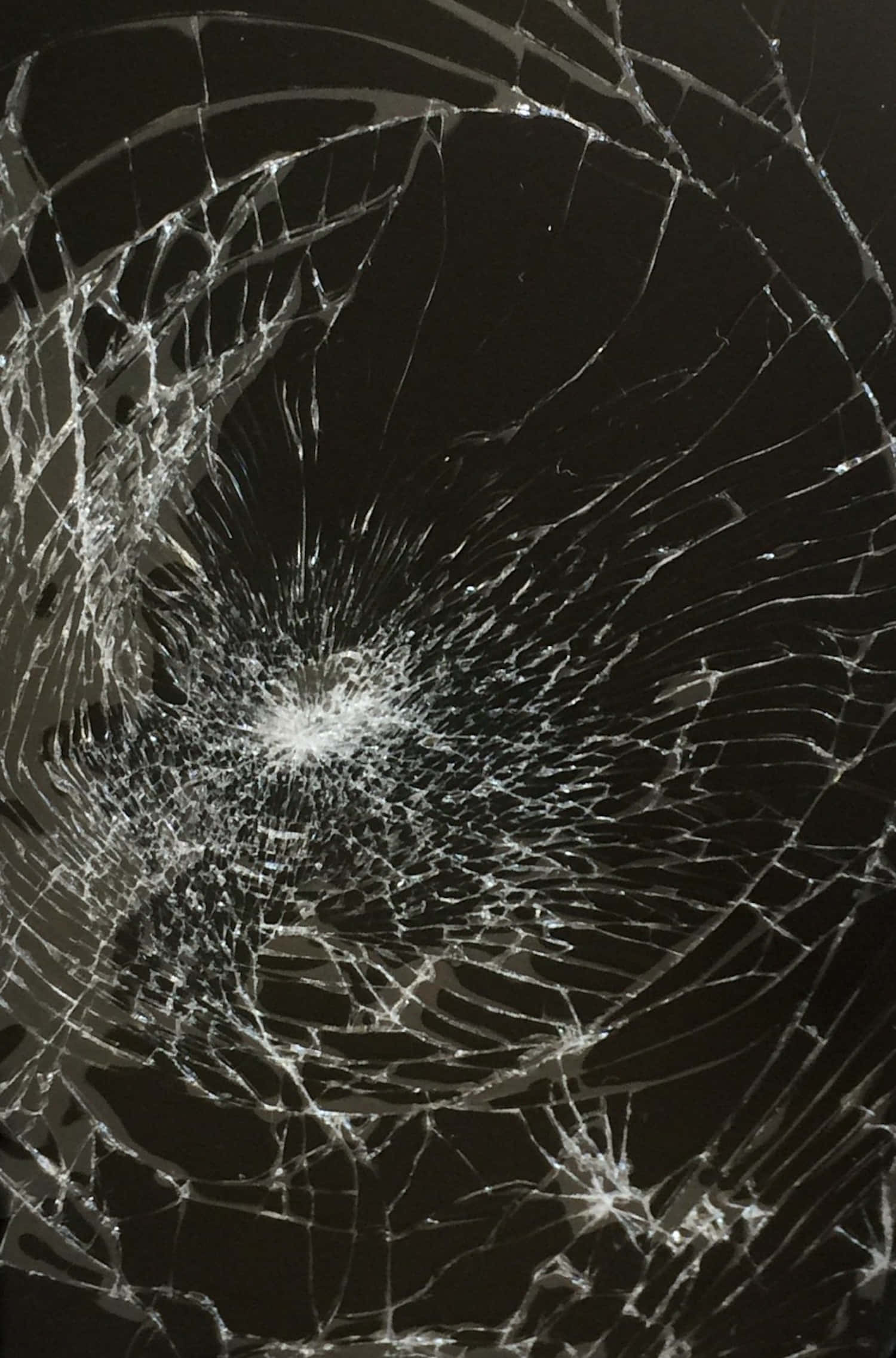 Fracture Glass 桌布 壁紙 — 特寫鏡頭，顯示一塊破碎玻璃，從中央撞擊點向外輻射出複雜裂紋，背景為深色。