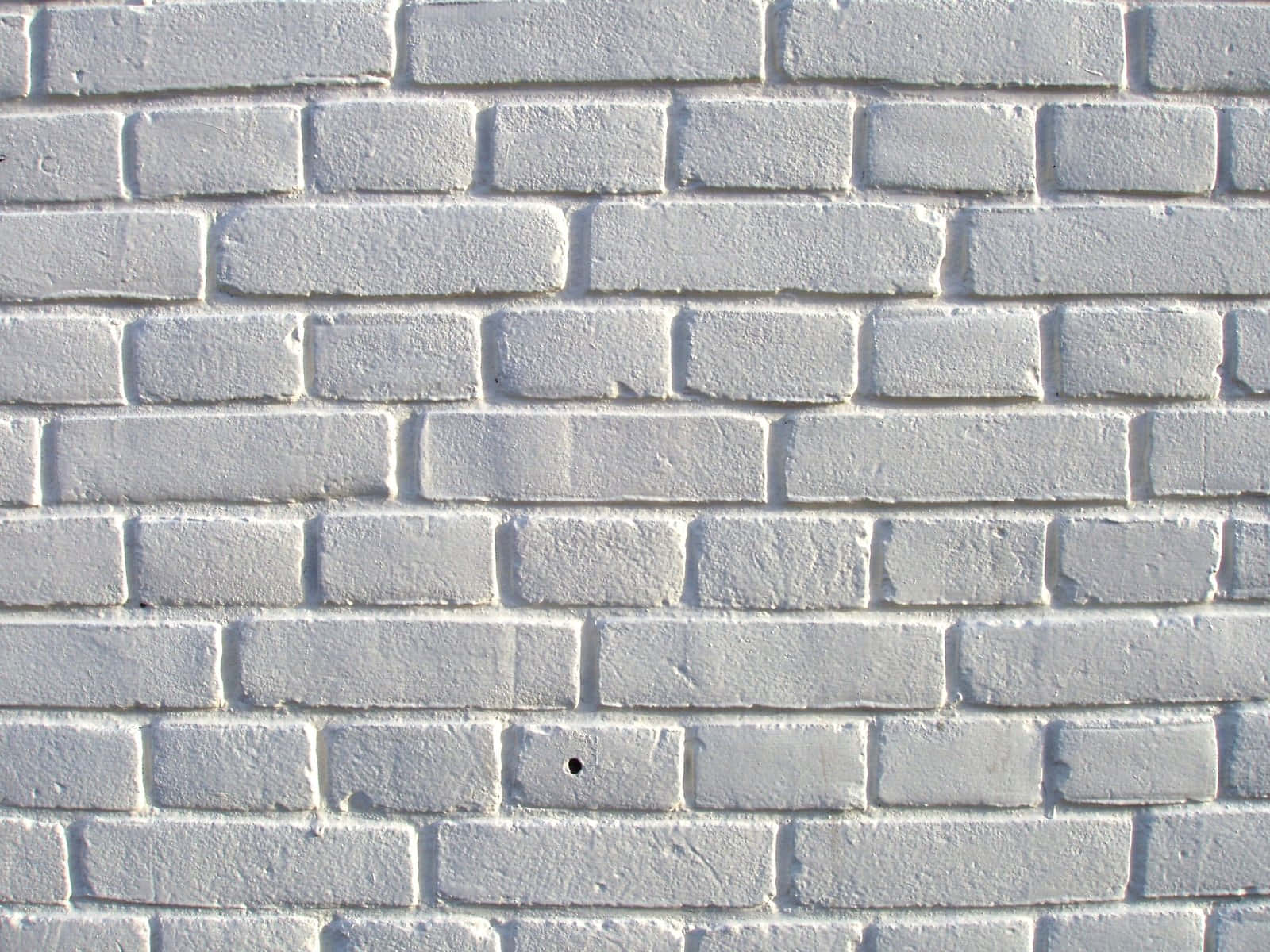 White Brick Wall 桌布 壁紙 — 特寫鏡頭，顯示一面風化的白色磚牆，可見砂漿線，其中一塊磚上有一個細小的黑色孔洞。