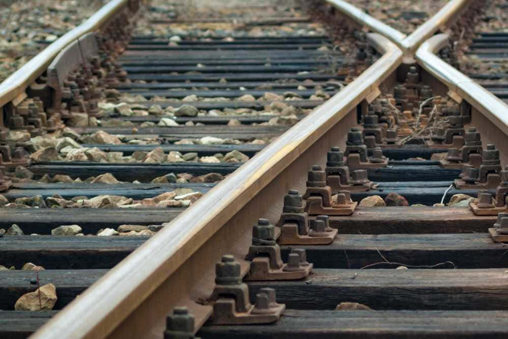 Train Tracks 桌布 壁紙 — 特寫鏡頭：風化的鐵路軌道在道岔處匯合，碎石道床和生鏽螺栓在柔和日光下。