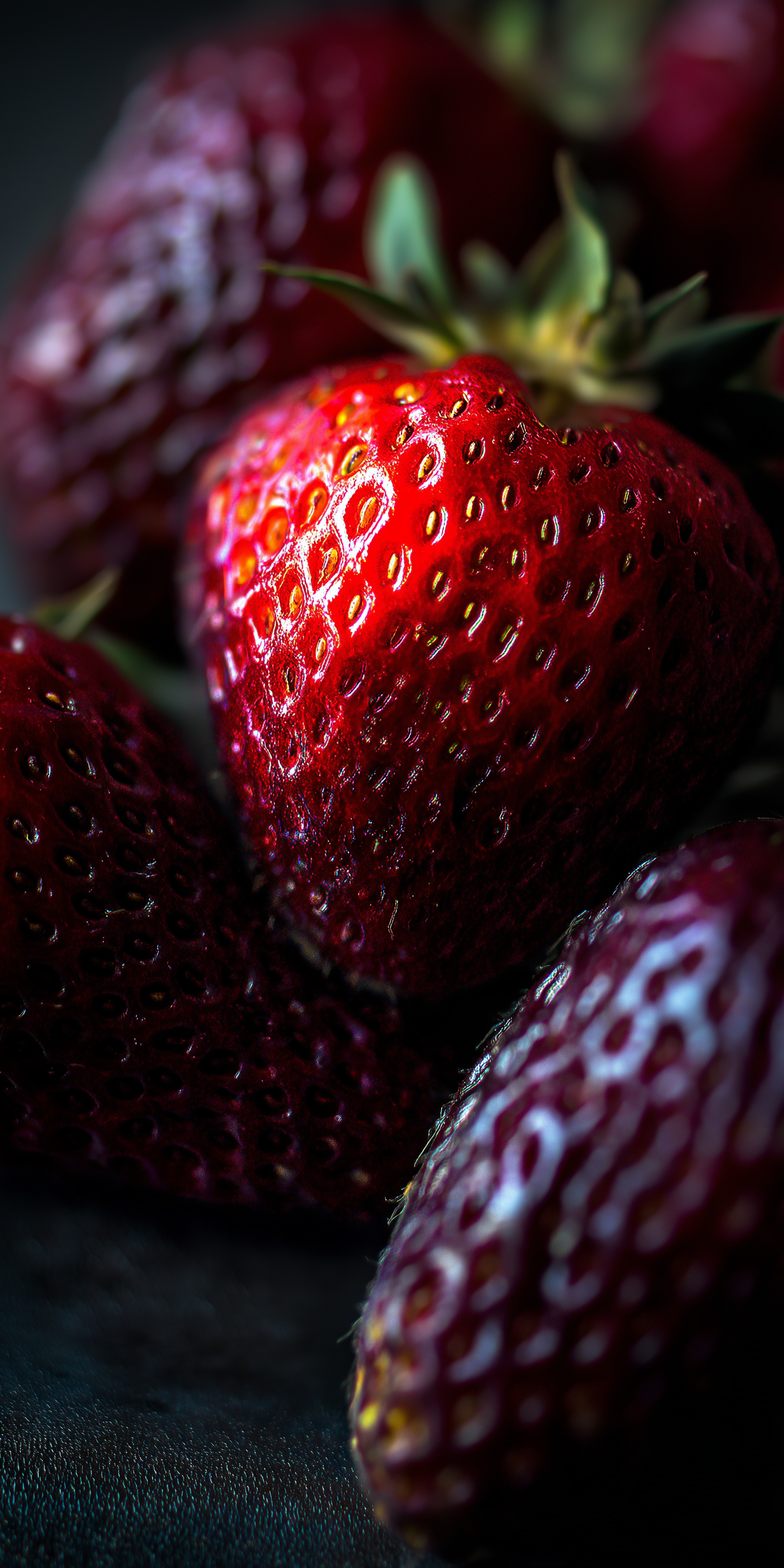Fruit 桌布 壁紙 — 特寫鏡頭，飽滿成熟的草莓，表面光滑鮮紅，帶有綠色葉子，背景深色。