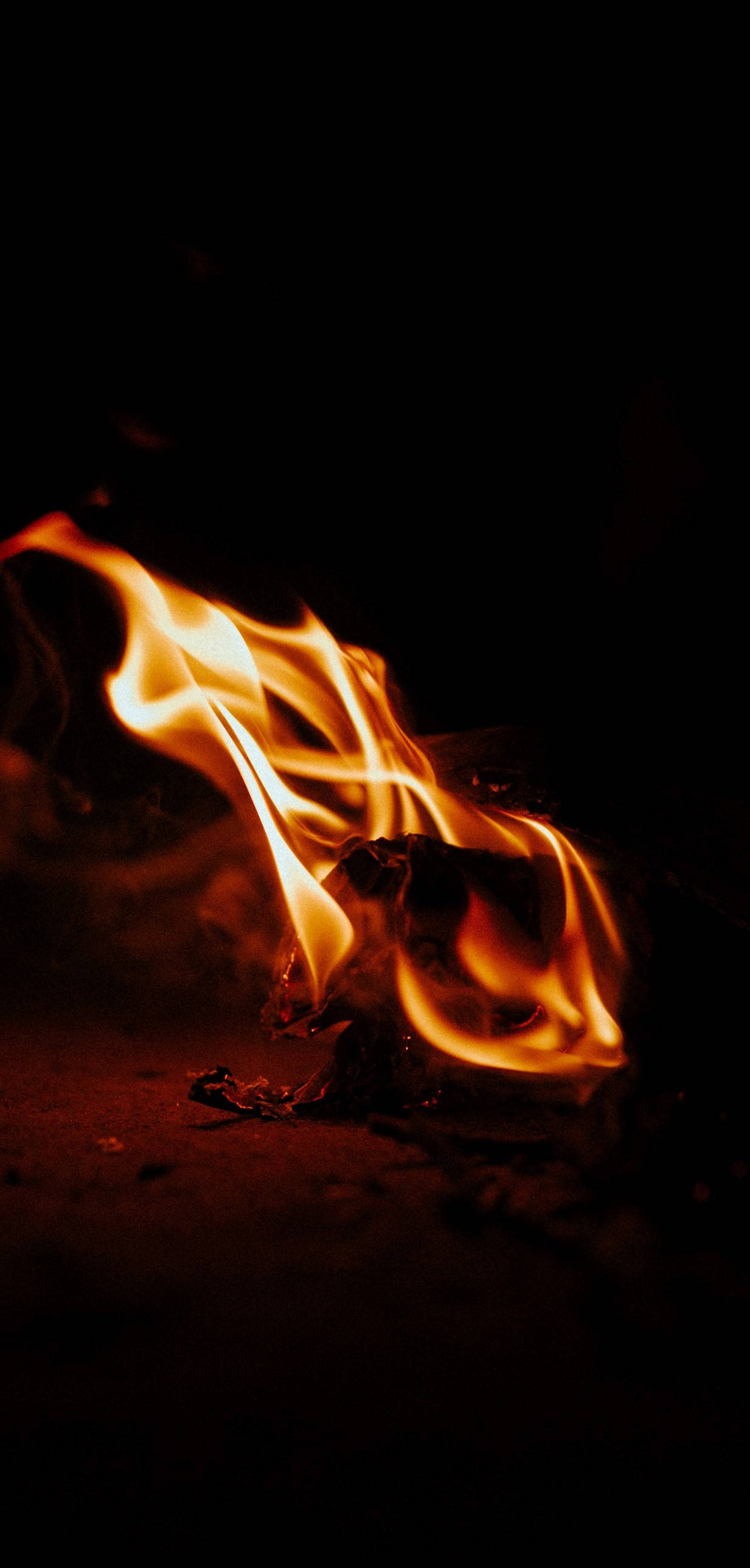 iPhone Fire 桌布 壁紙 — 特寫鏡頭，鮮豔的橙色和黃色火焰在深色燒焦的木頭上舞動，背景漆黑一片。