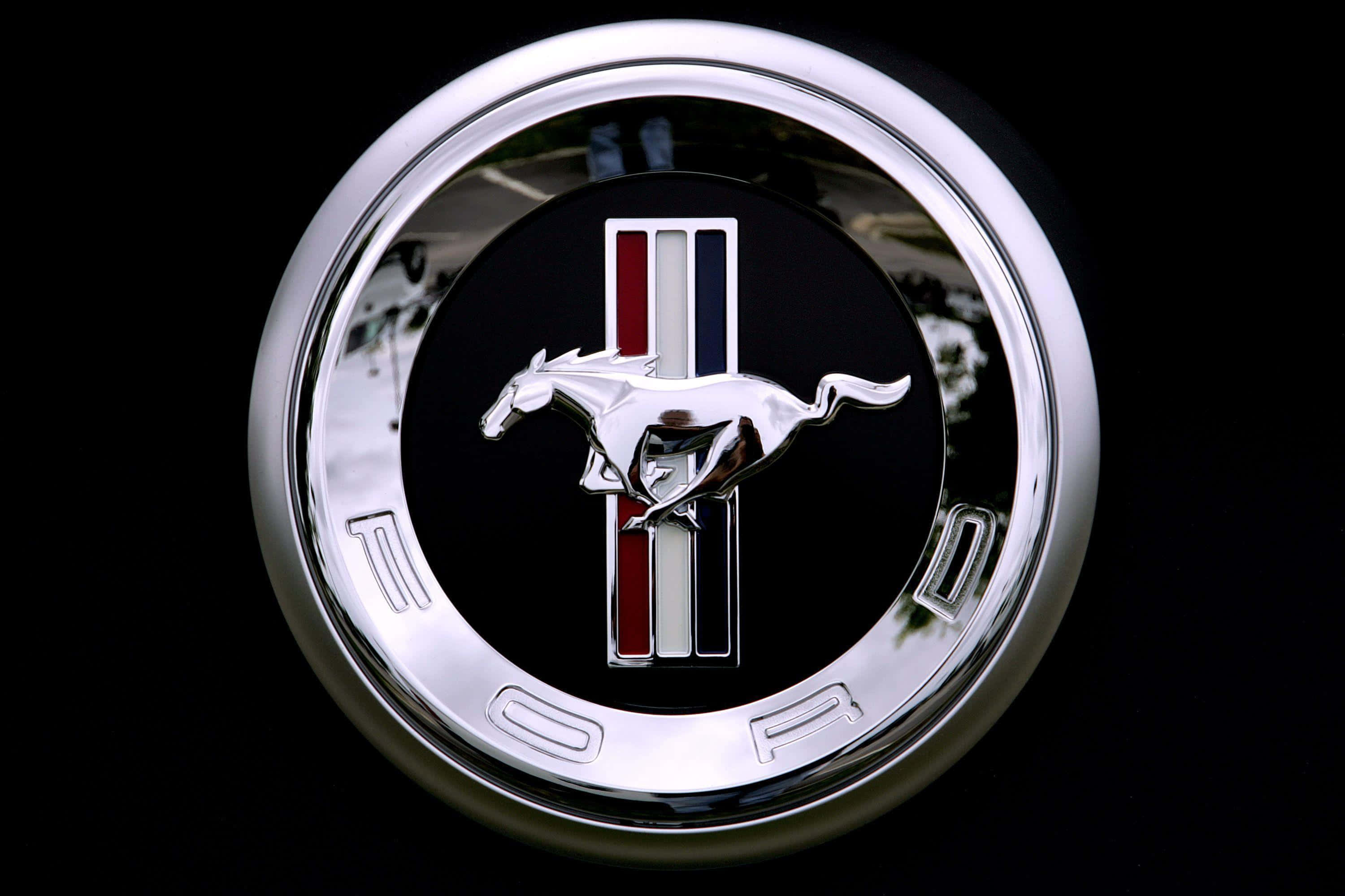 Car Logo 桌布 壁紙 — 特寫鏡頭：黑色背景上帶有紅、白、藍條紋的鍍鉻福特野馬徽章，圖案為奔騰的馬。