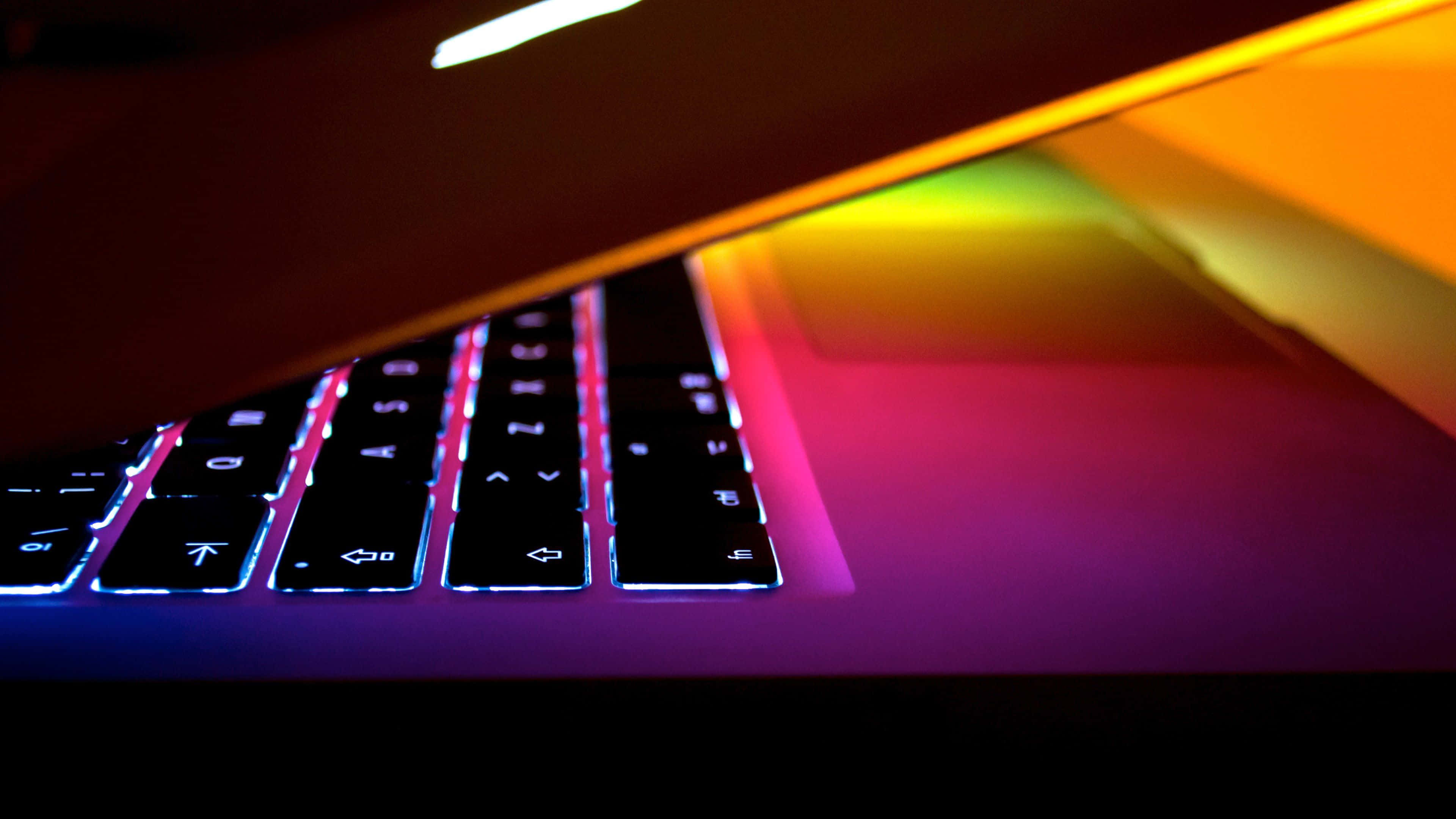 4K Apple 桌布 壁紙 — 特寫鏡頭顯示一個在黑暗背景下發出鮮豔彩虹背光的筆記型電腦鍵盤。