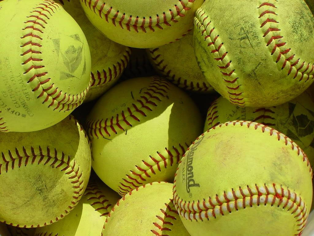 Cute Softball 桌布 壁紙 — 特寫鏡頭顯示磨損的黃色壘球，帶有紅色縫線，在明亮陽光下堆疊在一起。