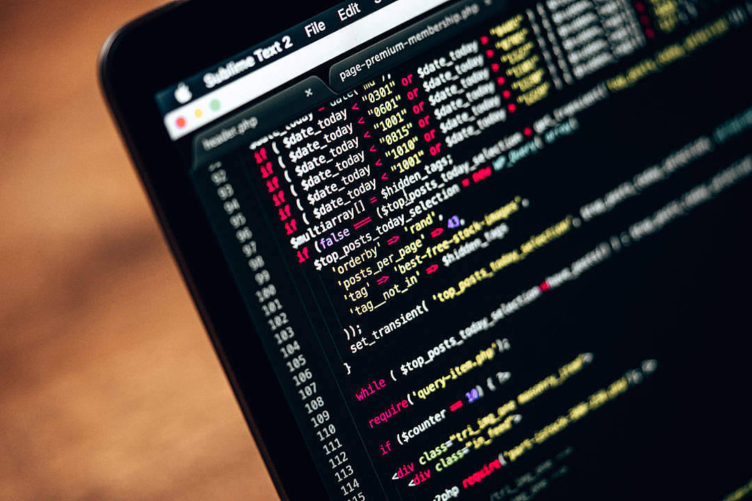 Website 桌布 壁紙 — 特寫鏡頭顯示筆記型電腦螢幕在 Sublime Text 2 中顯示色彩繽紛的 PHP 程式碼，背景為模糊的木桌。