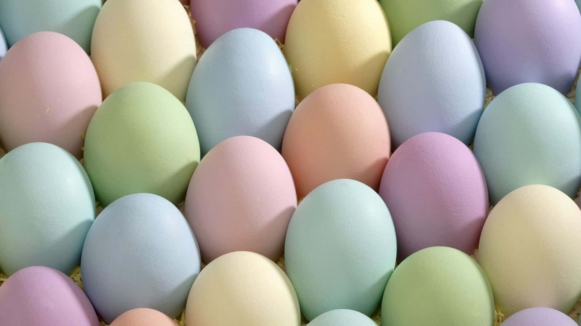 Pastel Easter 桌布 壁紙 — 特寫鏡頭顯示粉彩色的雞蛋放在稻草中，展現粉紅、藍、綠和黃色的柔和色調。