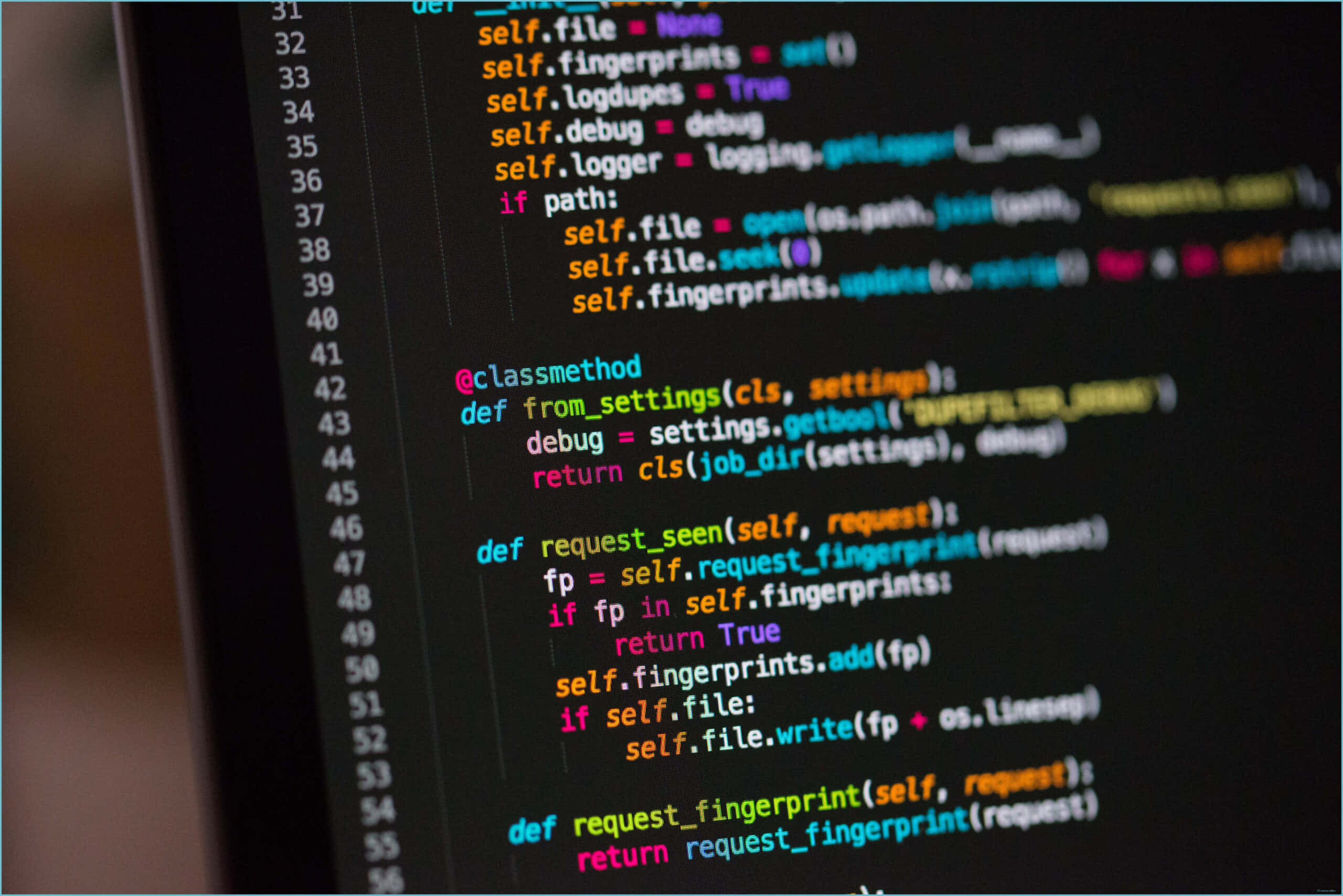 It Computer 桌布 壁紙 — 特寫鏡頭顯示色彩繽紛的 Python 程式碼在深色顯示器螢幕上滾動，背景模糊。