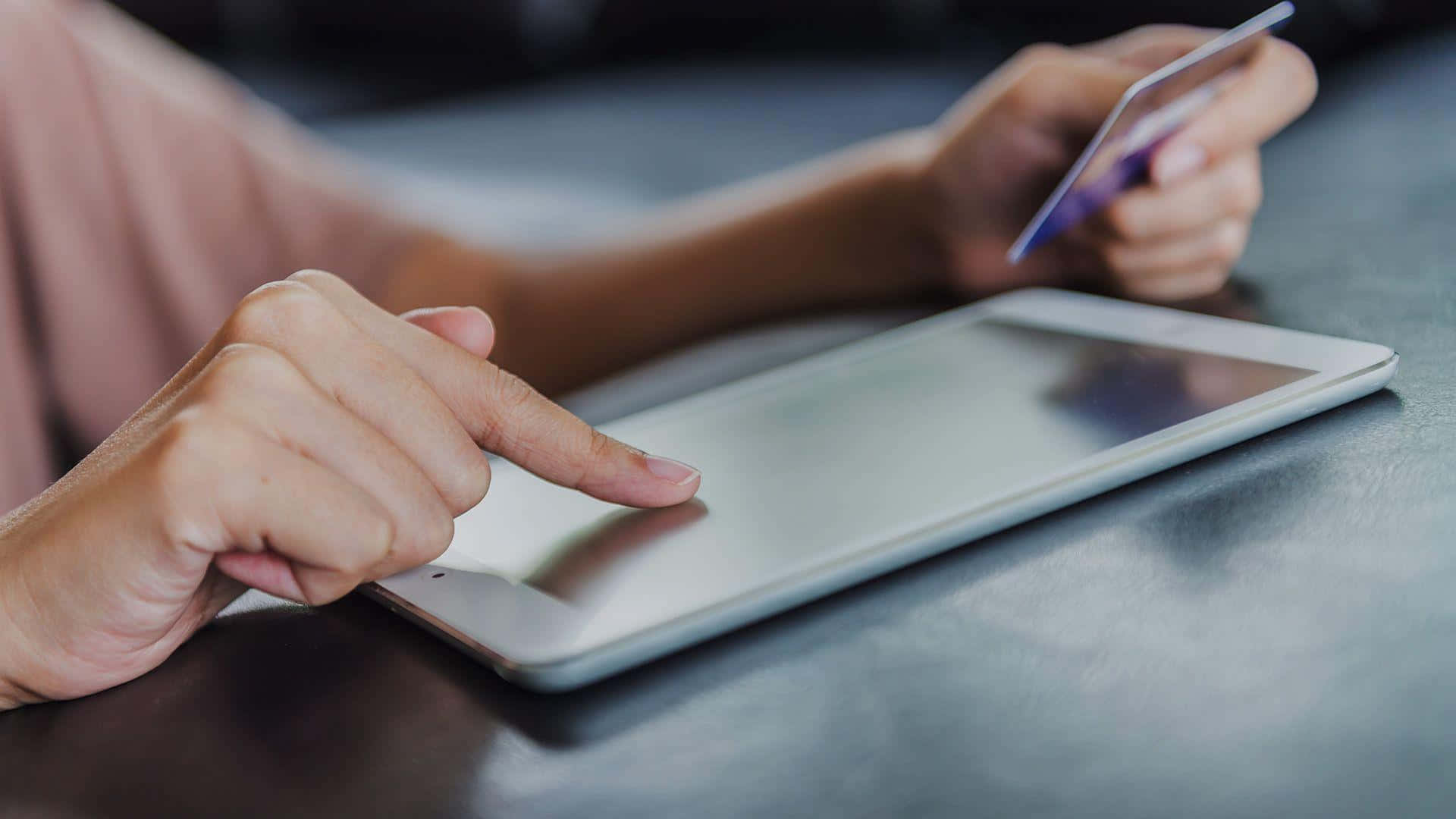 E Commerce 桌布 壁紙 — 特寫雙手在深色桌子上使用平板電腦並手持信用卡進行線上付款。