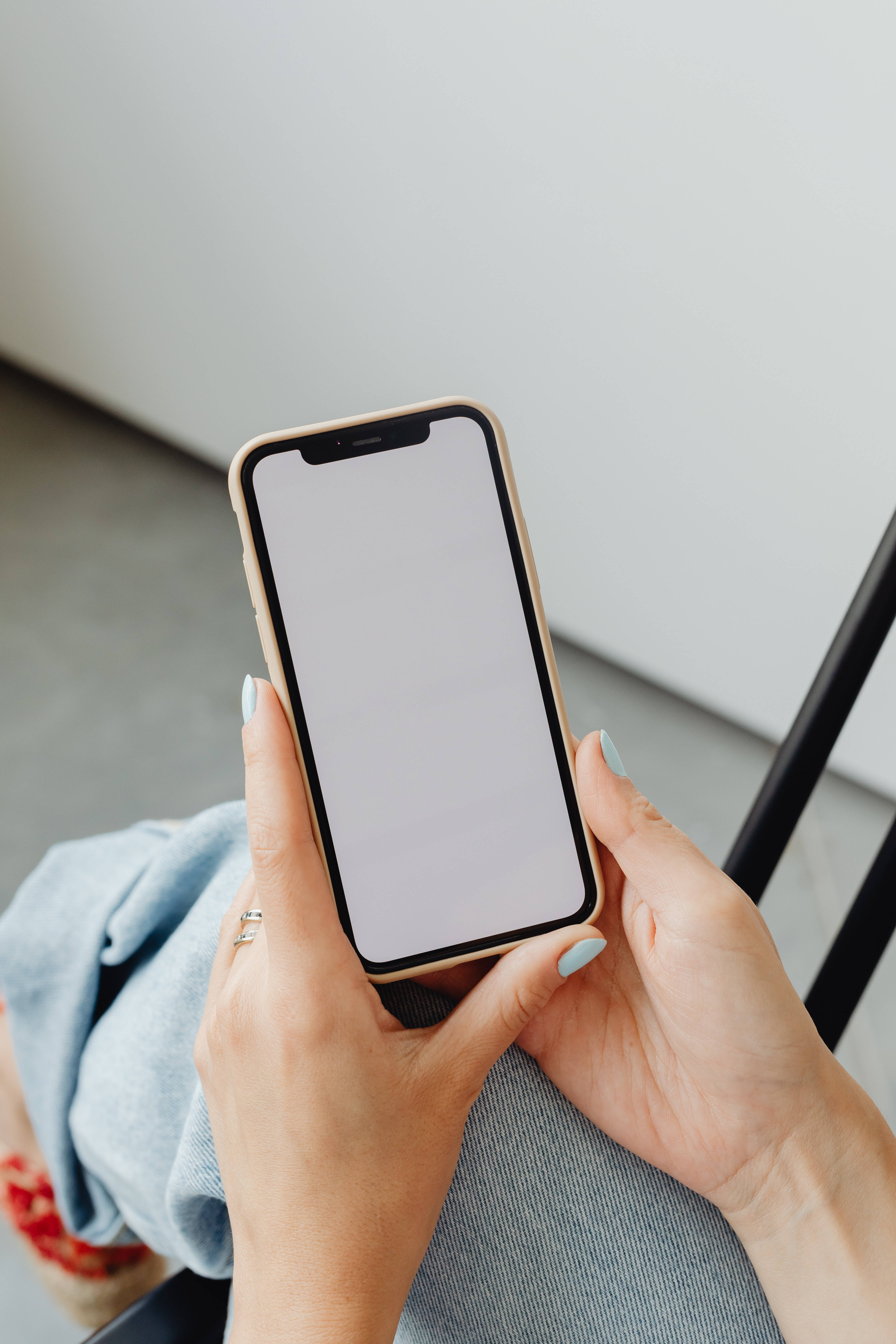 酷炫iPhone 桌布 壁紙 — 特寫雙手拿著空白螢幕的智慧型手機，背景為簡約室內環境。