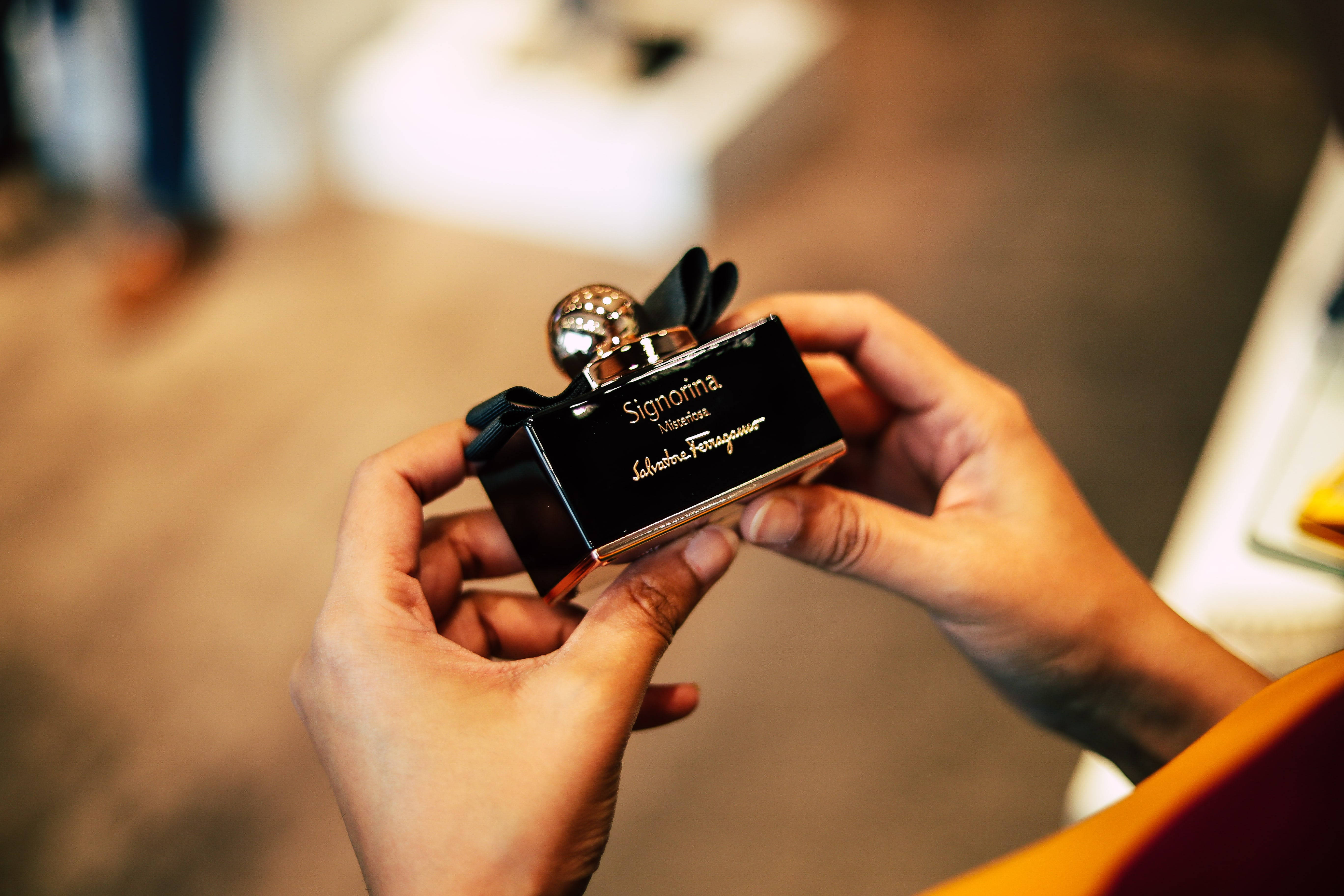 Ferragamo 桌布 壁紙 — 特寫雙手拿著黑色 Salvatore Ferragamo Signorina 香水瓶，帶有金色點綴和閃閃發光的瓶蓋。