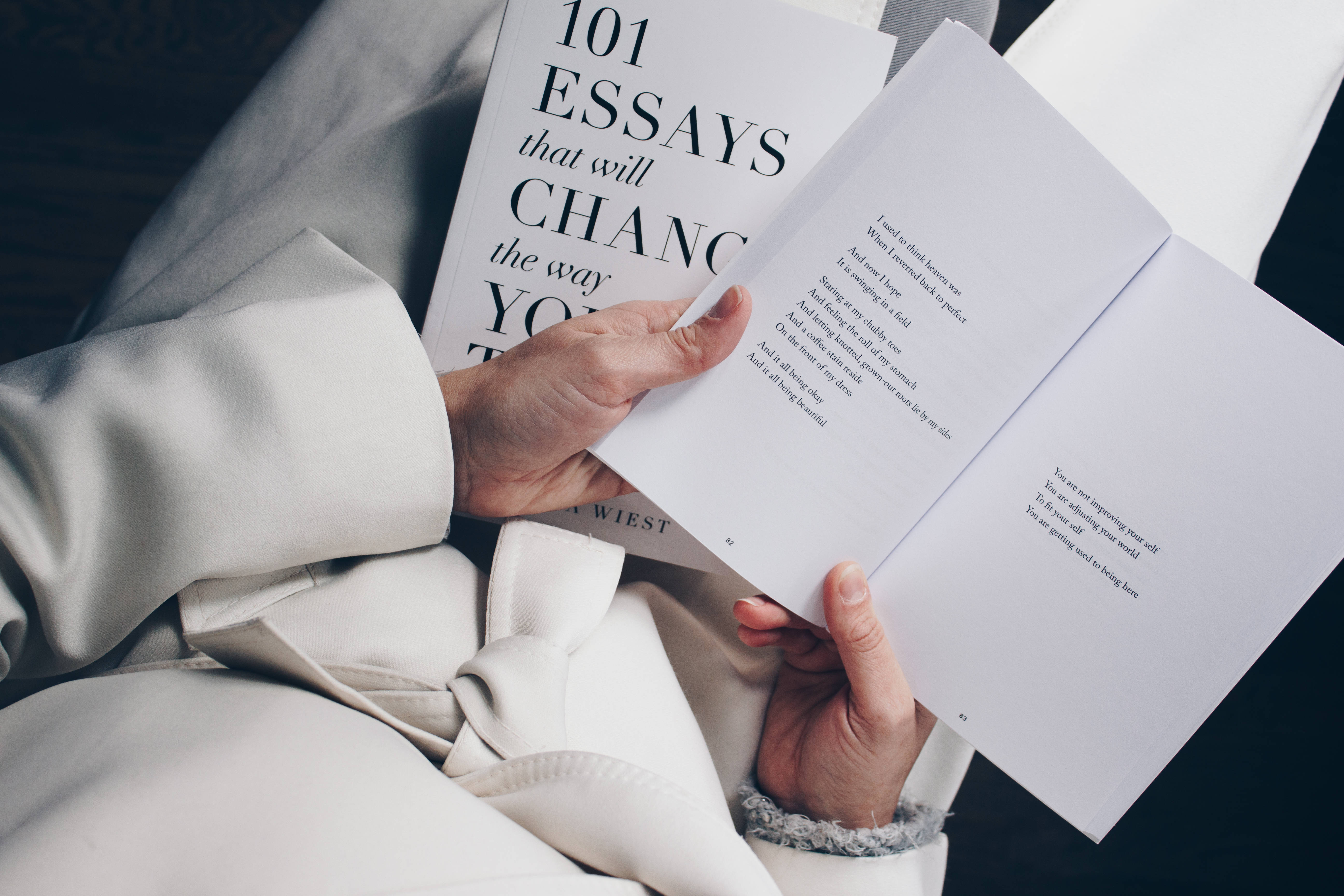 Studying 桌布 壁紙 — 特寫雙手捧著一本打開的書，書名為101 Essays that will Change the Way You Think，同時裹著舒適的白色浴袍。