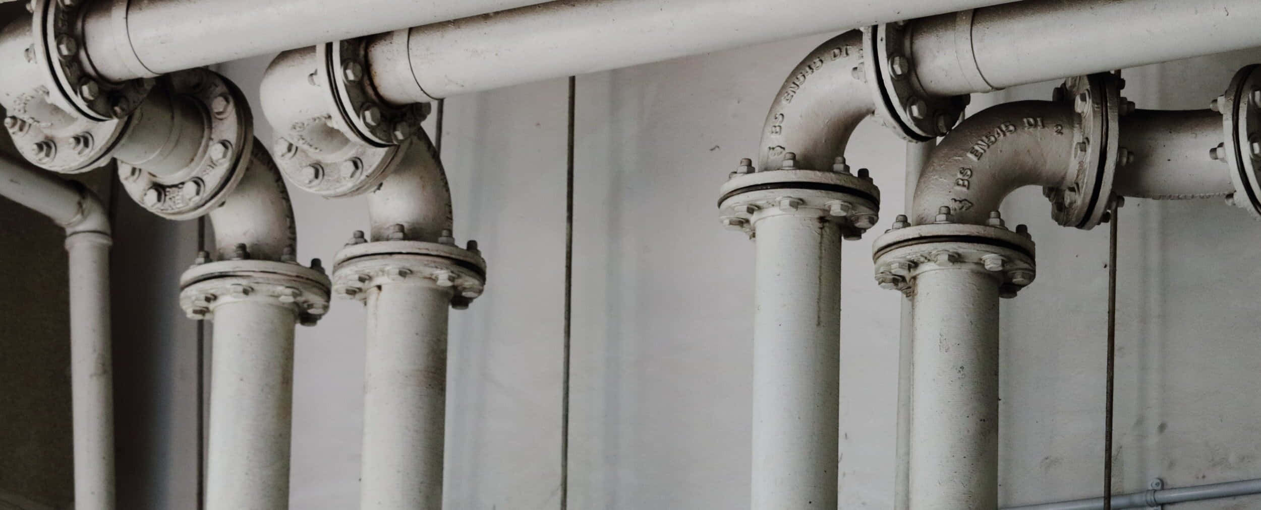 Plumbing 桌布 壁紙 — 特寫風化白色工業管道，帶有螺栓法蘭，靠著素色牆壁。