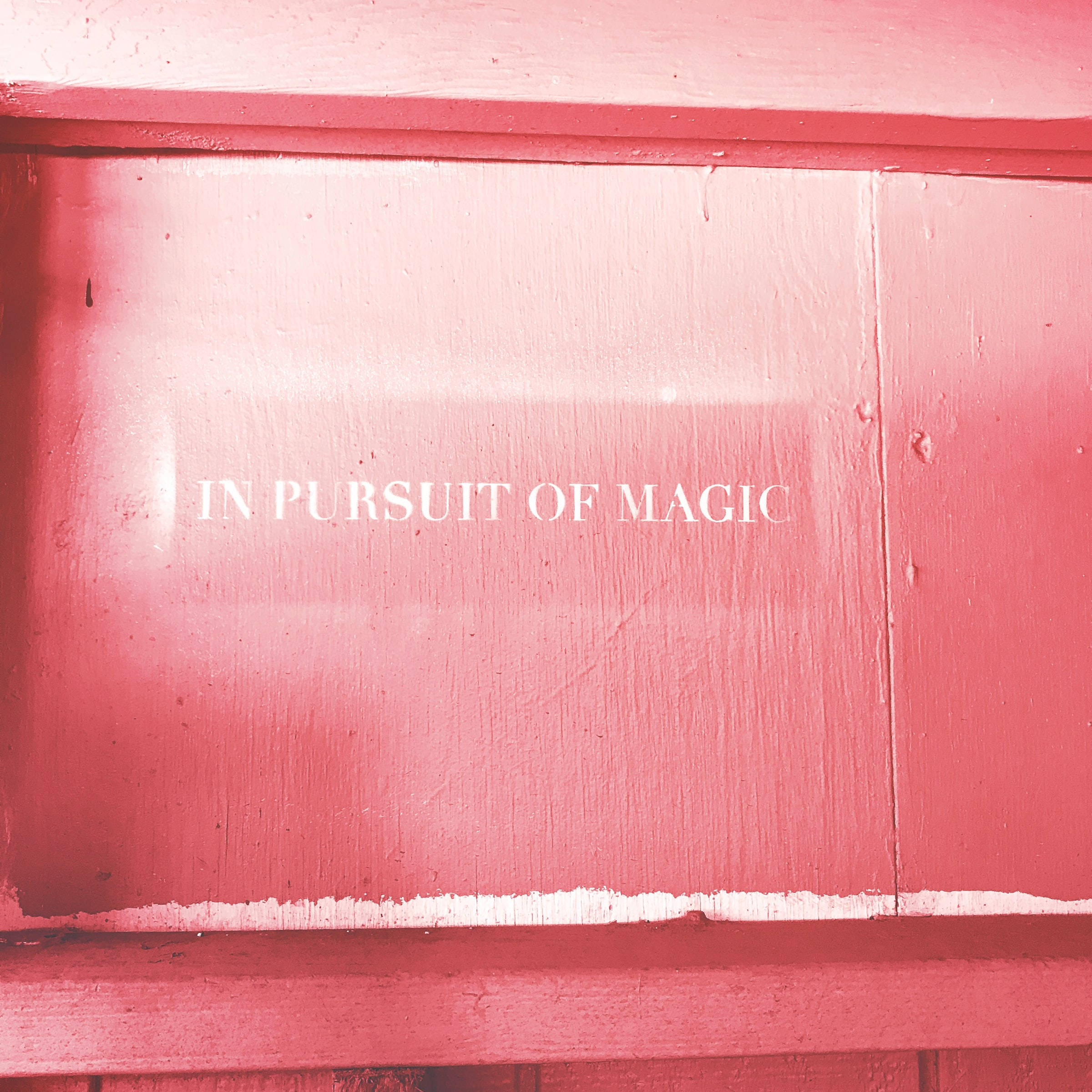 粉紅色 桌布 壁紙 — 特寫風化的粉紅色木板上帶有白色文字「IN PURSUIT OF MAGIC」，在柔和燈光下。