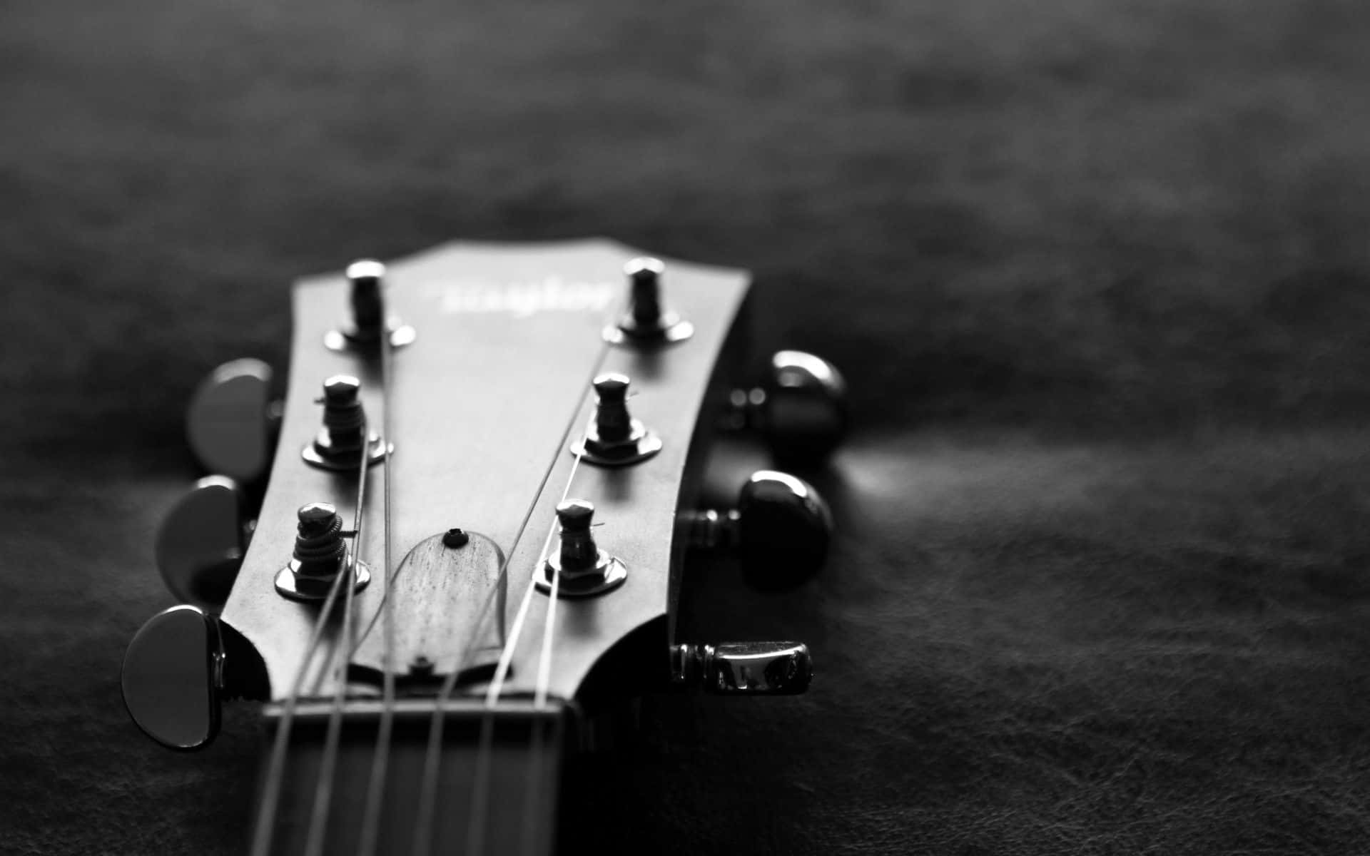 Black And White Music 桌布 壁紙 — 特寫黑白拍攝，吉他琴頭帶有調音旋鈕和琴弦，背景為紋理深色背景。
