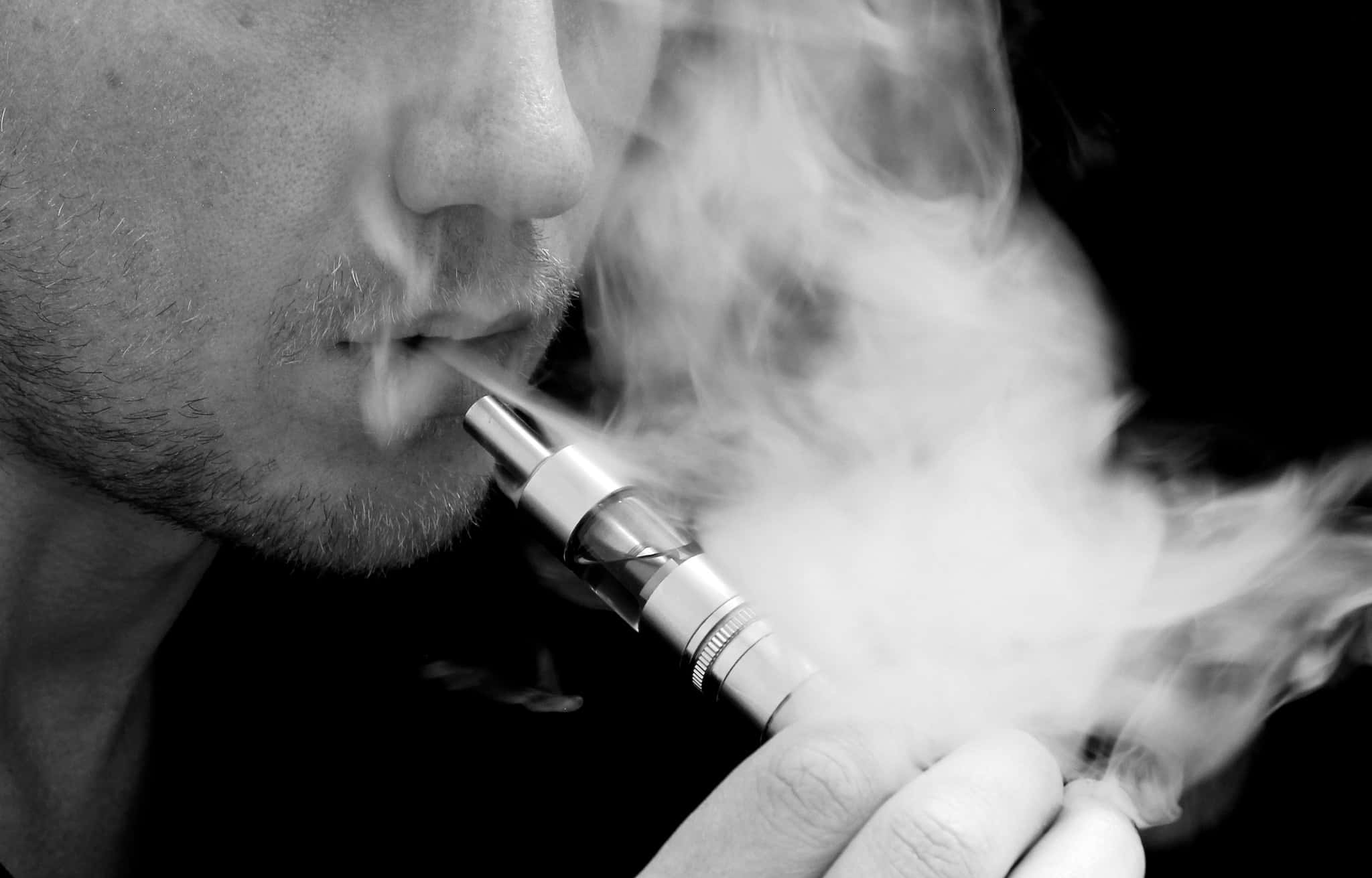 Vape 桌布 壁紙 — 特寫黑白照片，一名男子在黑暗背景下呼出電子煙的濃厚煙霧。