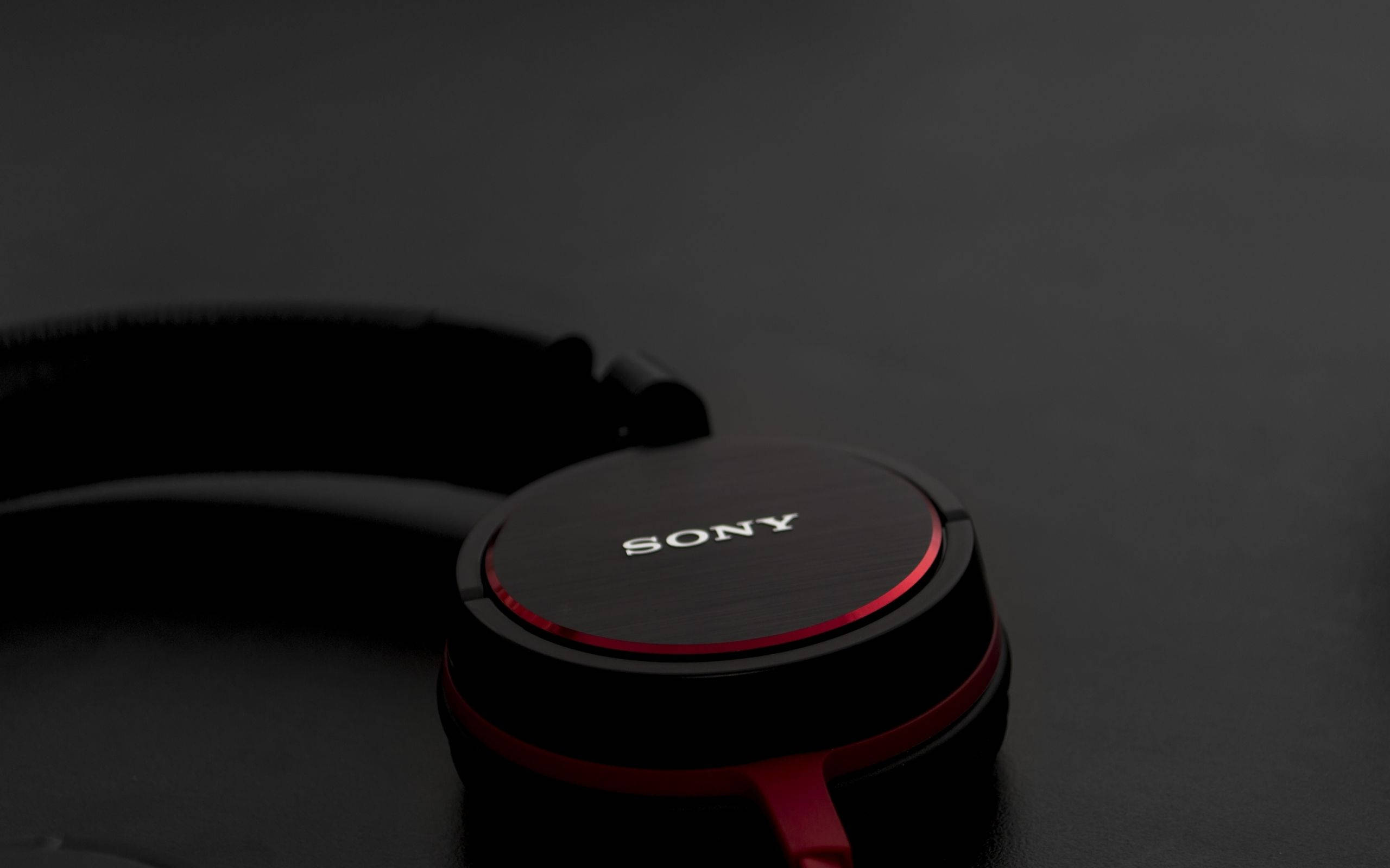 Sony 桌布 壁紙 — 特寫黑色Sony耳機，帶有紅色點綴，在柔和燈光下放置在深色表面上。