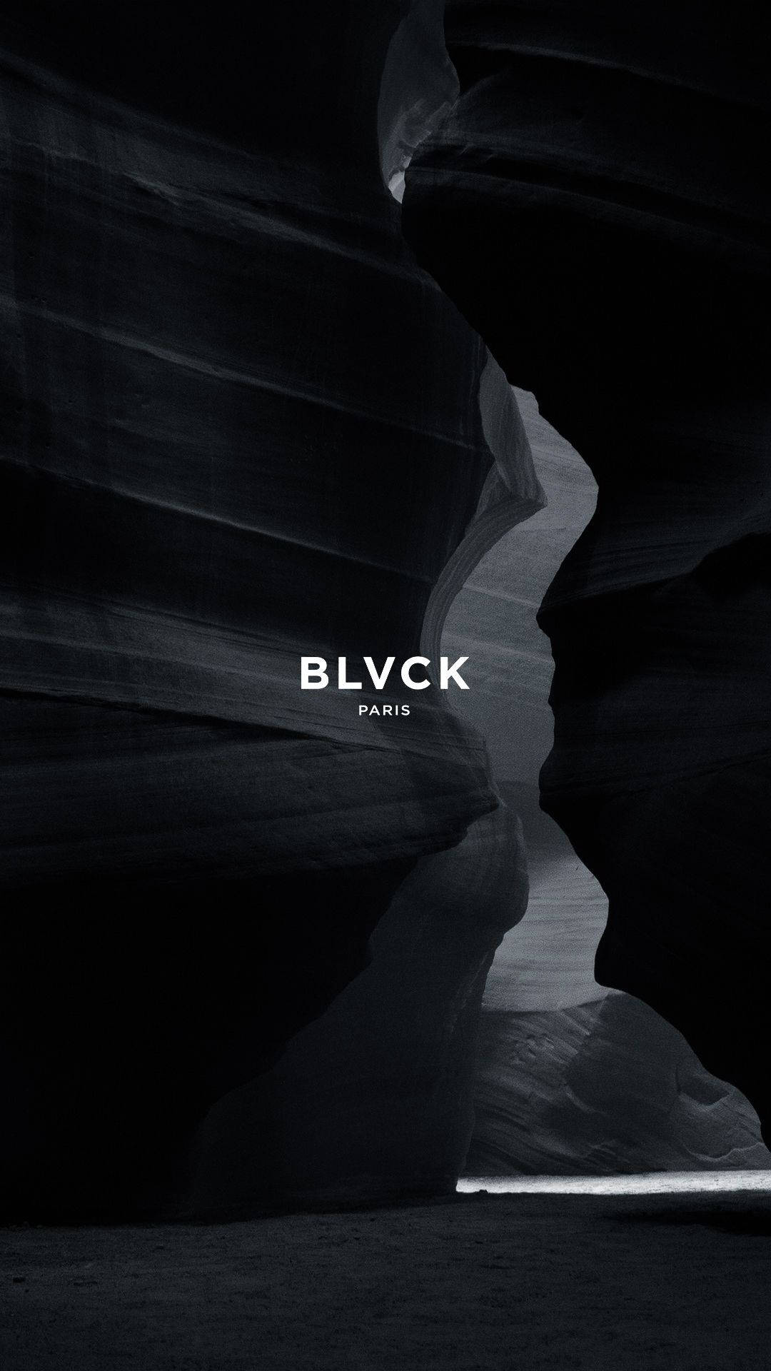 Blvck Paris 桌布 壁紙 — 狹窄峽谷的戲劇性黑白景觀，擁有平滑彎曲的岩壁，盡頭透出一線明亮的光芒。