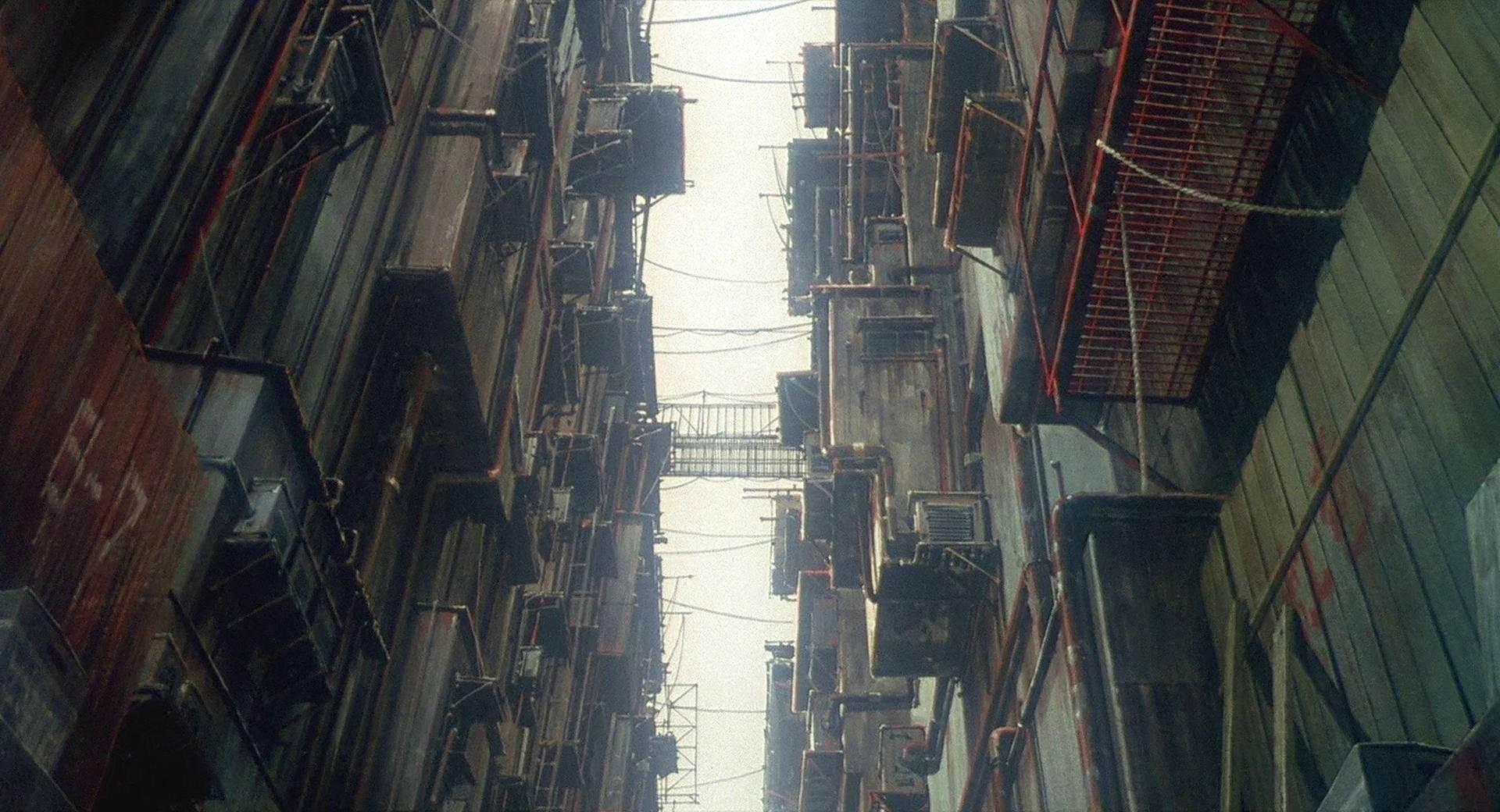 攻殼機動隊 桌布 壁紙 — 狹窄的城市小巷，兩旁是風化的建築物，掛著電線，遠處有橋樑，天空多雲。