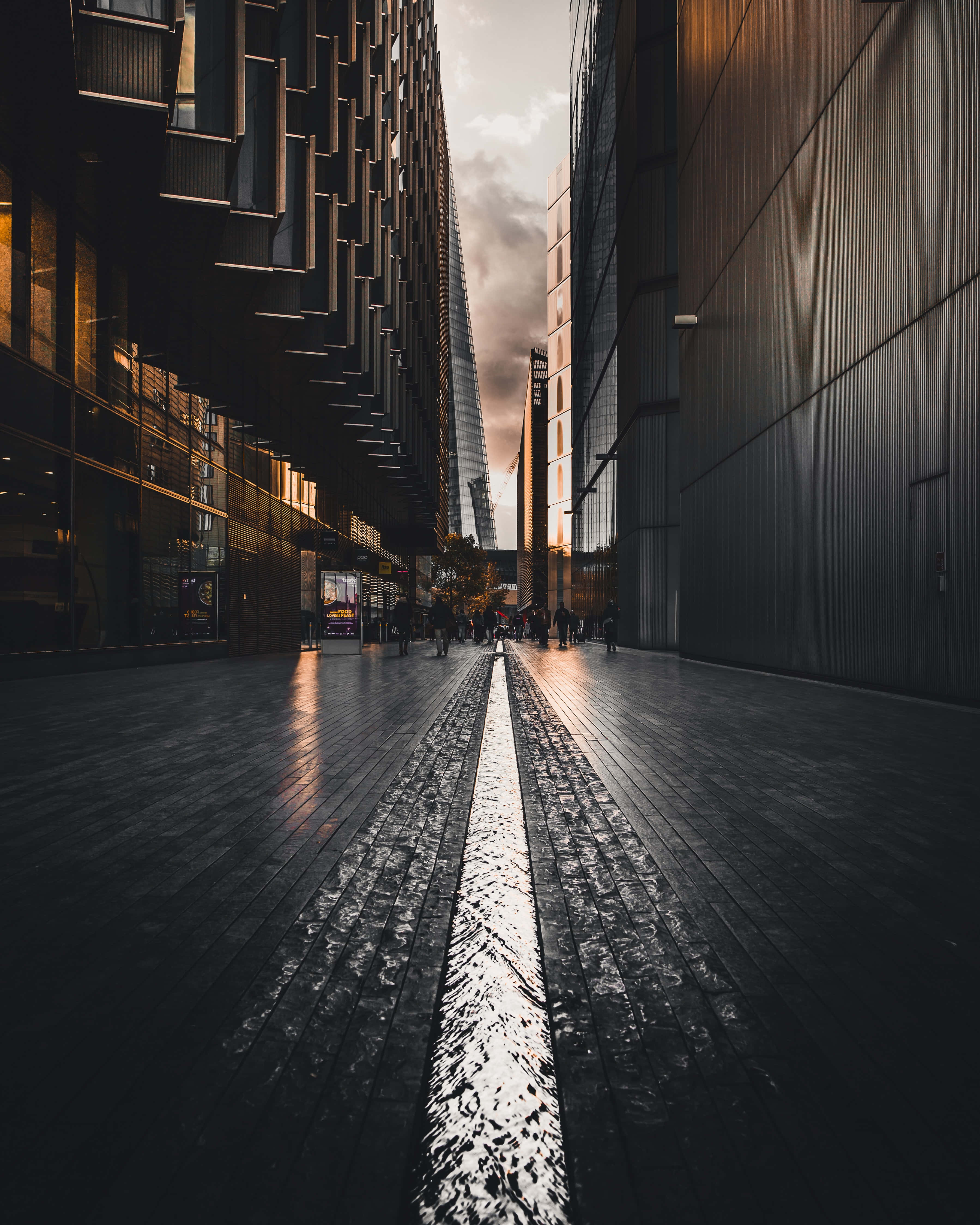 Street 桌布 壁紙 — 狹窄的城市小巷，兩旁是高聳的現代建築，濕漉漉的路面反射著金色的日落光芒。