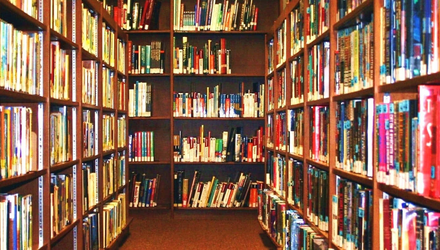 閱讀 桌布 壁紙 — 狹窄的通道，兩旁是高聳的木製書架，書架上擺滿了色彩繽紛的書籍，沐浴在溫暖的環境光中。