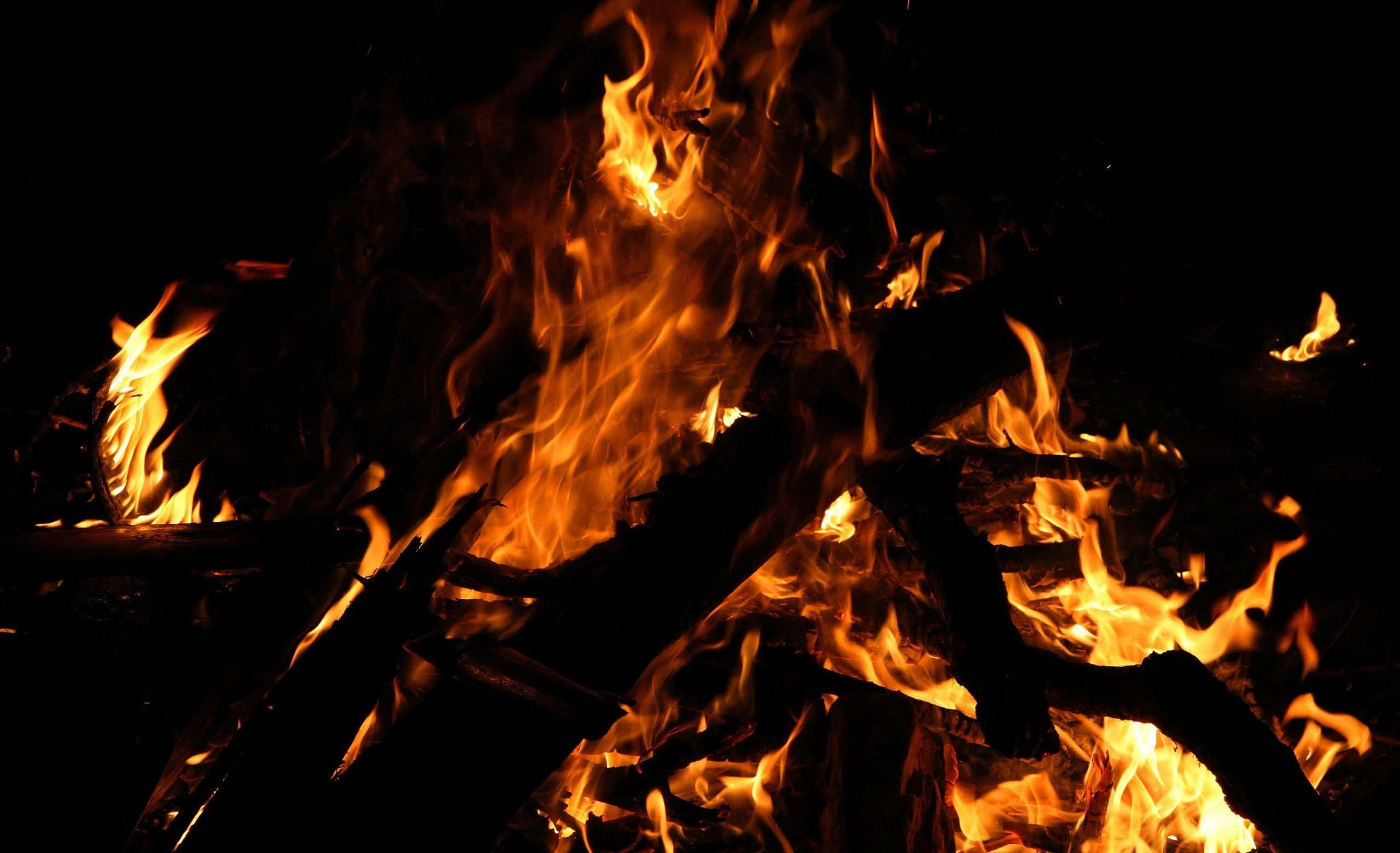 Campfire 桌布 壁紙 — 猛烈的火焰在漆黑的夜空下，於焦黑的木頭上跳躍並發出劈啪聲。