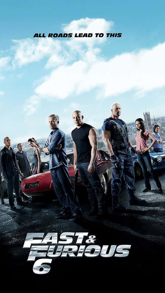 Fast And Furious Desktop 桌布 壁紙 — 《玩命關頭6》演員自信地站在紅色和藍色肌肉車旁，背景是明亮的天空和城市景觀。