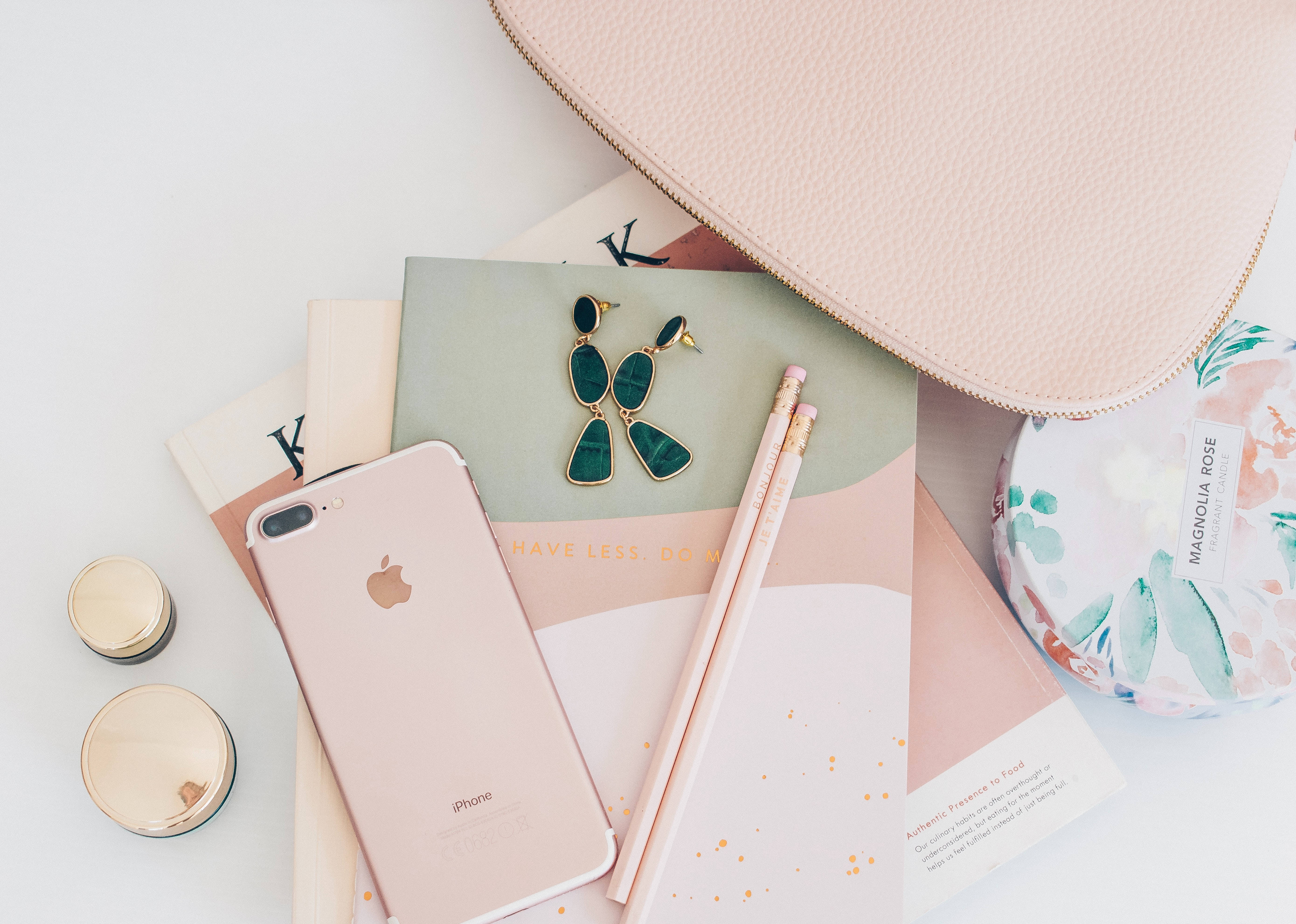 酷炫iPhone 桌布 壁紙 — 玫瑰金 iPhone、筆記本、鉛筆和花卉配件在柔軟白色表面上平鋪擺放。