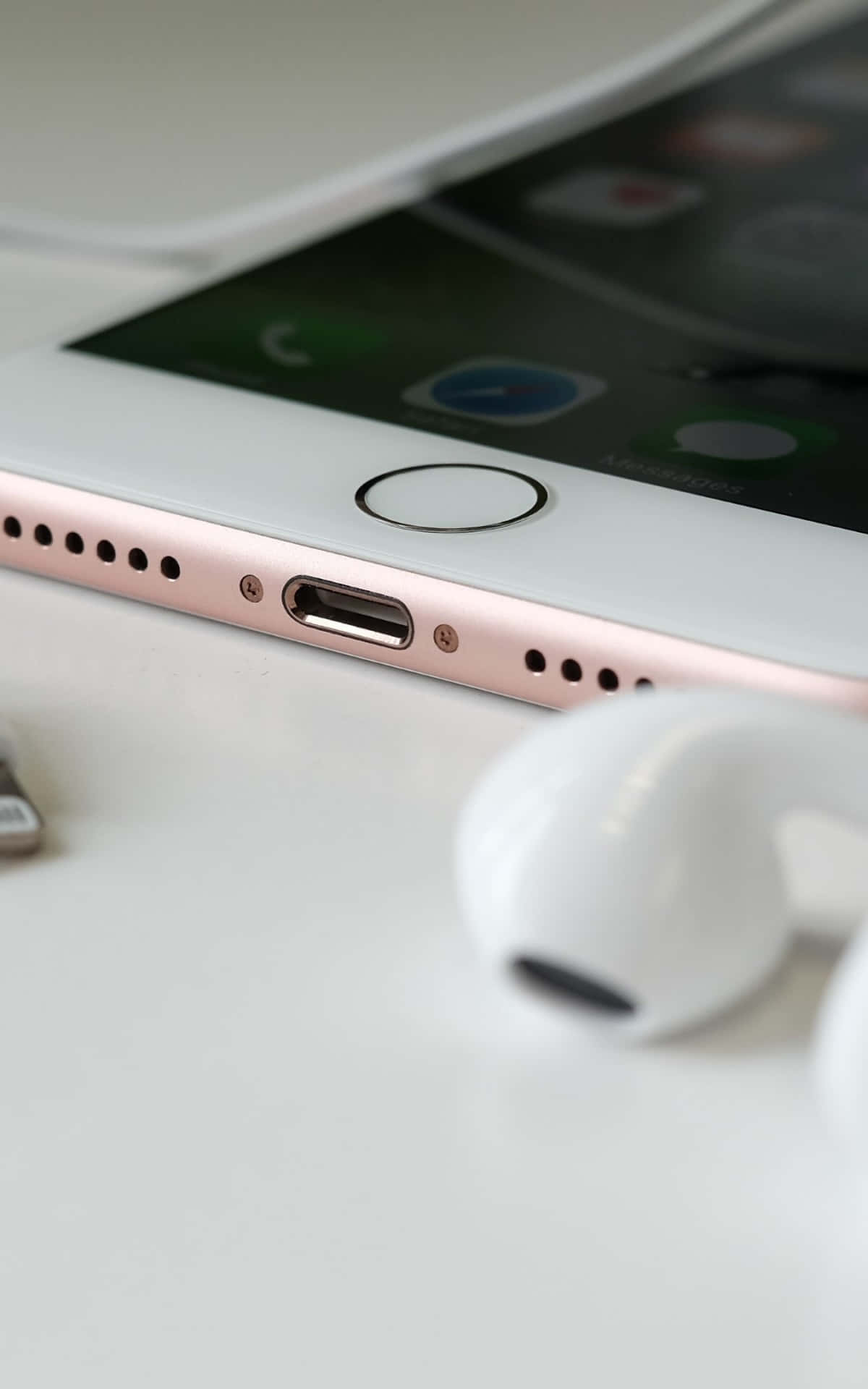 桌布 壁紙 — 玫瑰金iPhone搭配白色耳機的特寫，放置在潔白表面上。