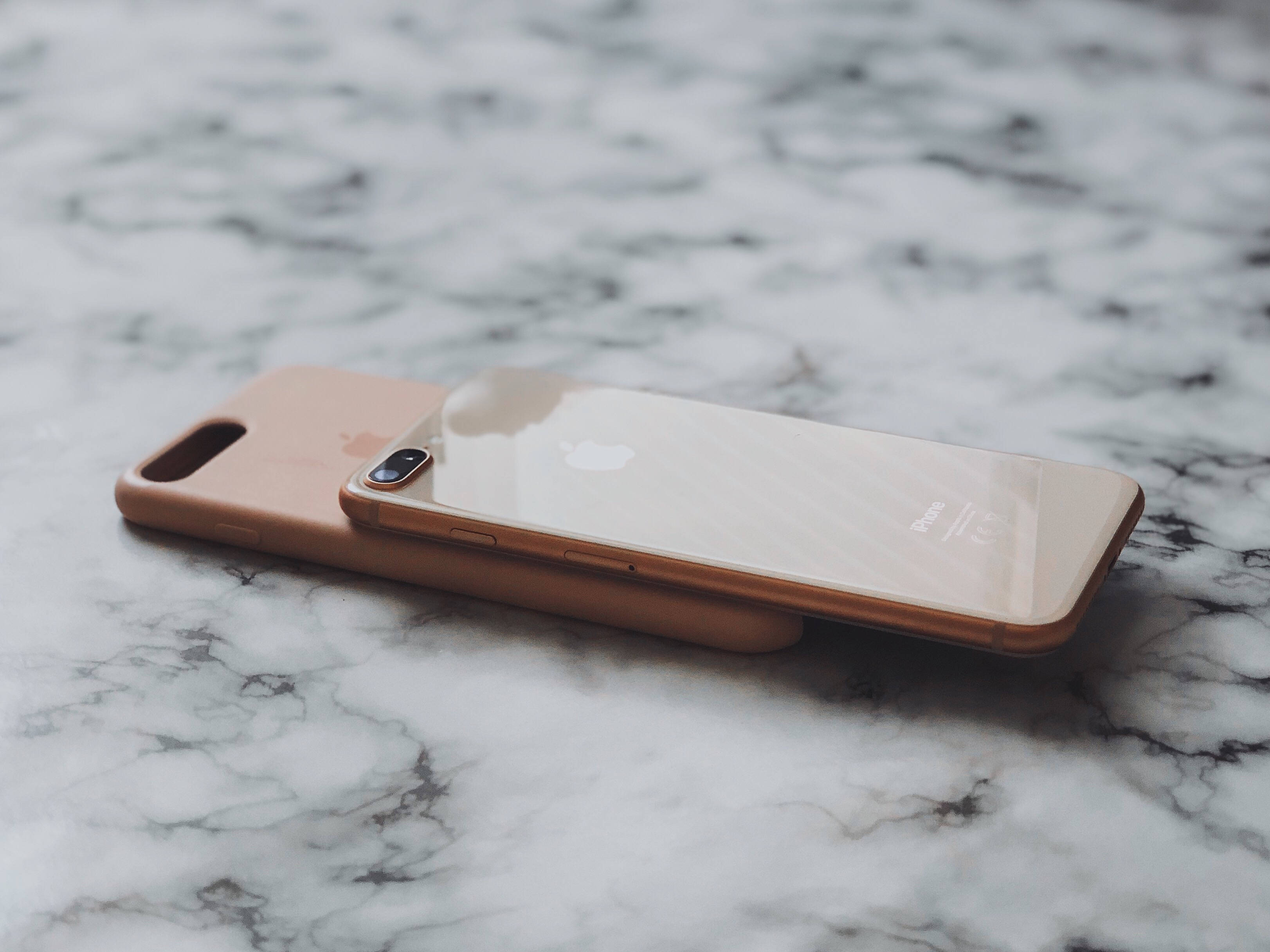 iPhone 8 桌布 壁紙 — 玫瑰金色iPhone放在相配的保護殼上，置於白色和灰色大理石表面，柔和自然光線照射。