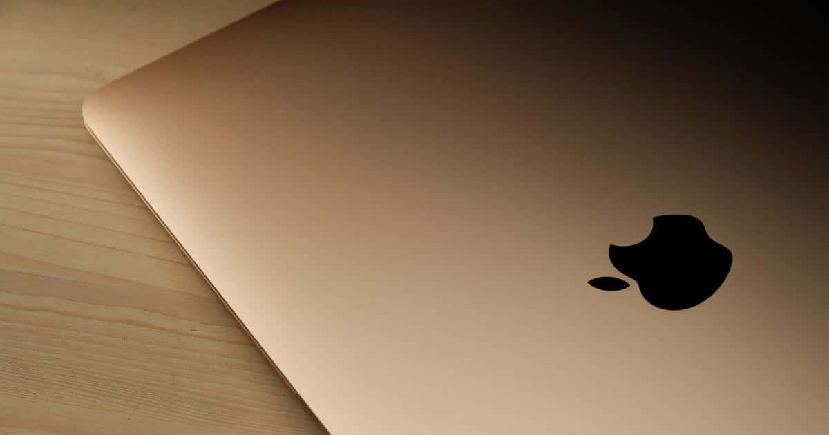 Mac 桌布 壁紙 — 玫瑰金色筆記型電腦帶有黑色Apple標誌，在柔和燈光下斜放在淺色木質表面上。