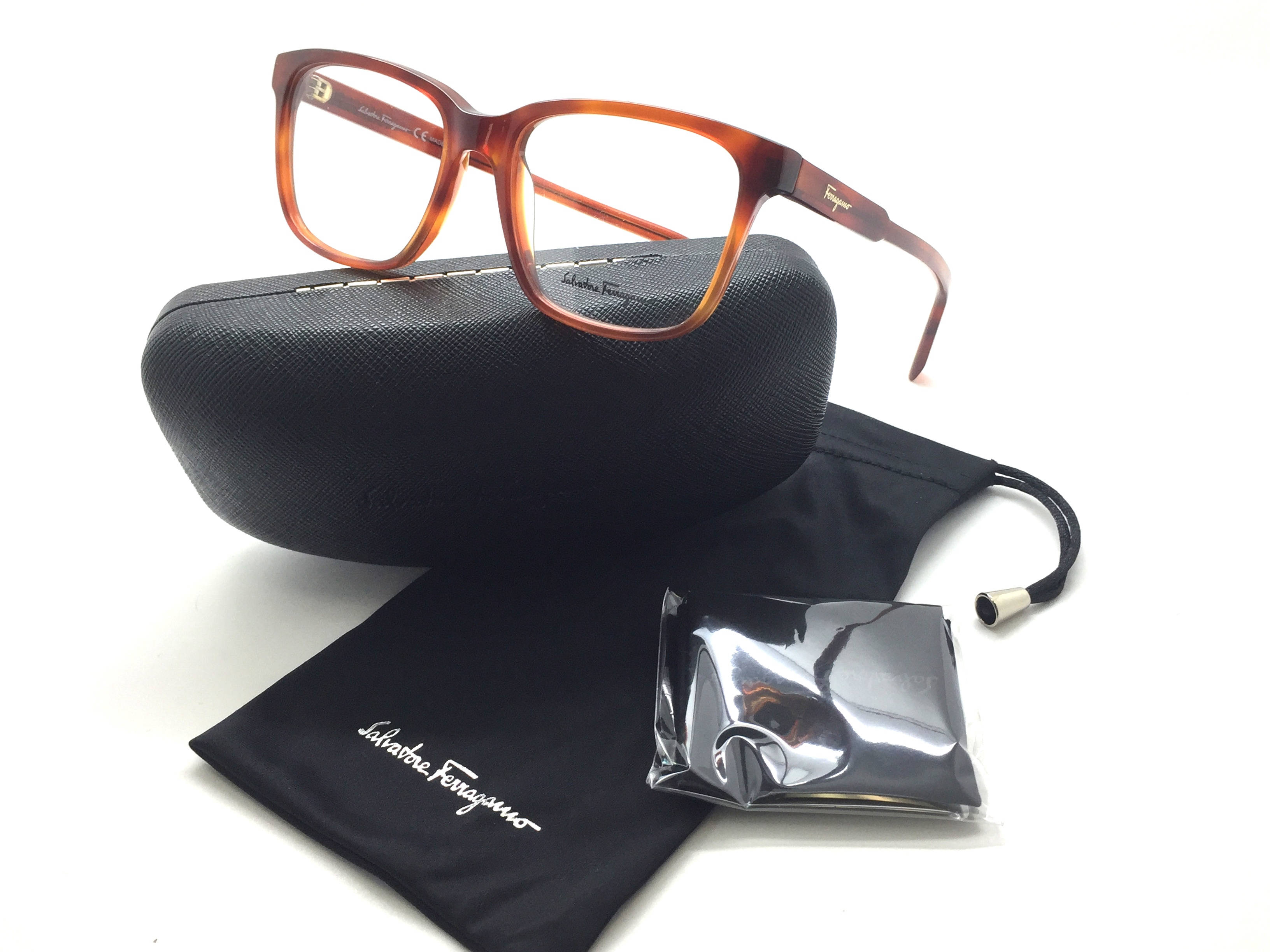 Ferragamo 桌布 壁紙 — 玳瑁眼鏡放在黑色眼鏡盒上，旁邊有品牌布和密封清潔套裝，背景為白色。