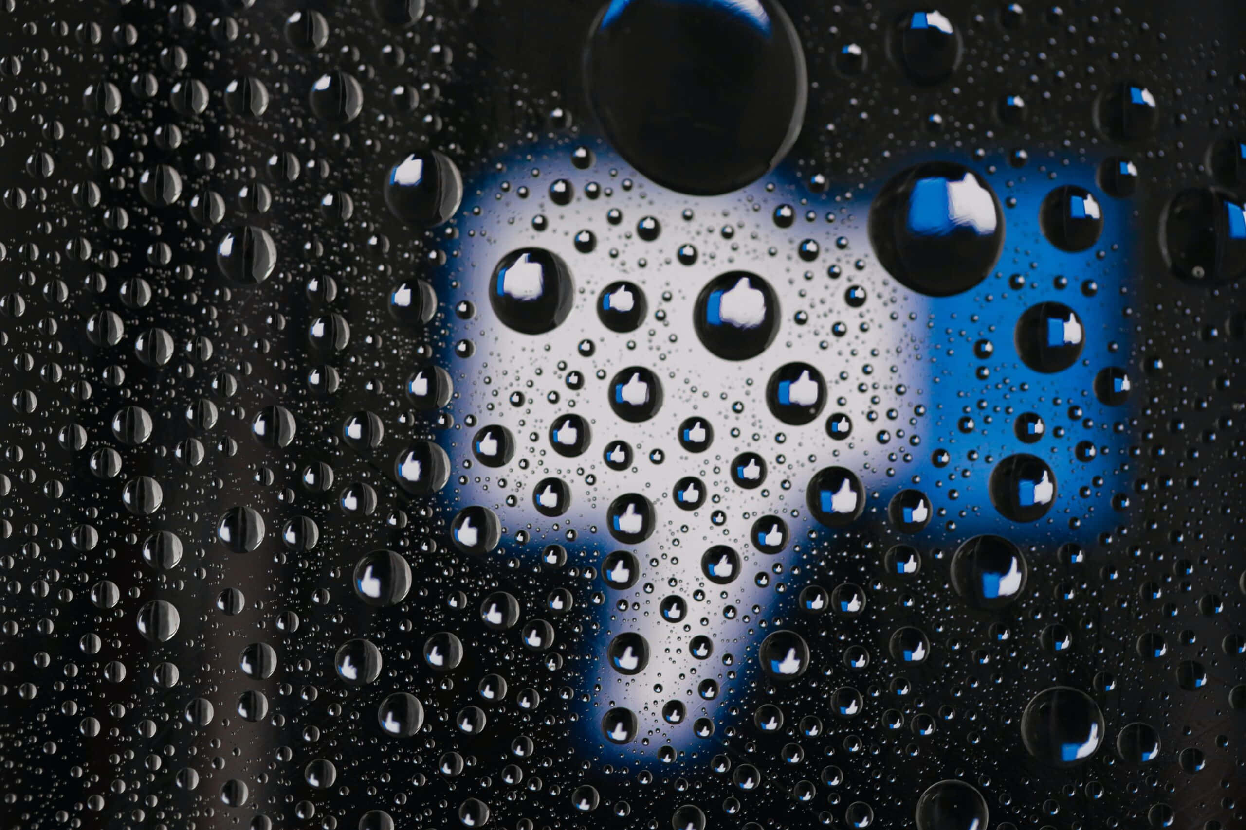 Raindrops 桌布 壁紙 — 玻璃上的雨滴扭曲了背景中模糊的藍白豎起大拇指圖示。