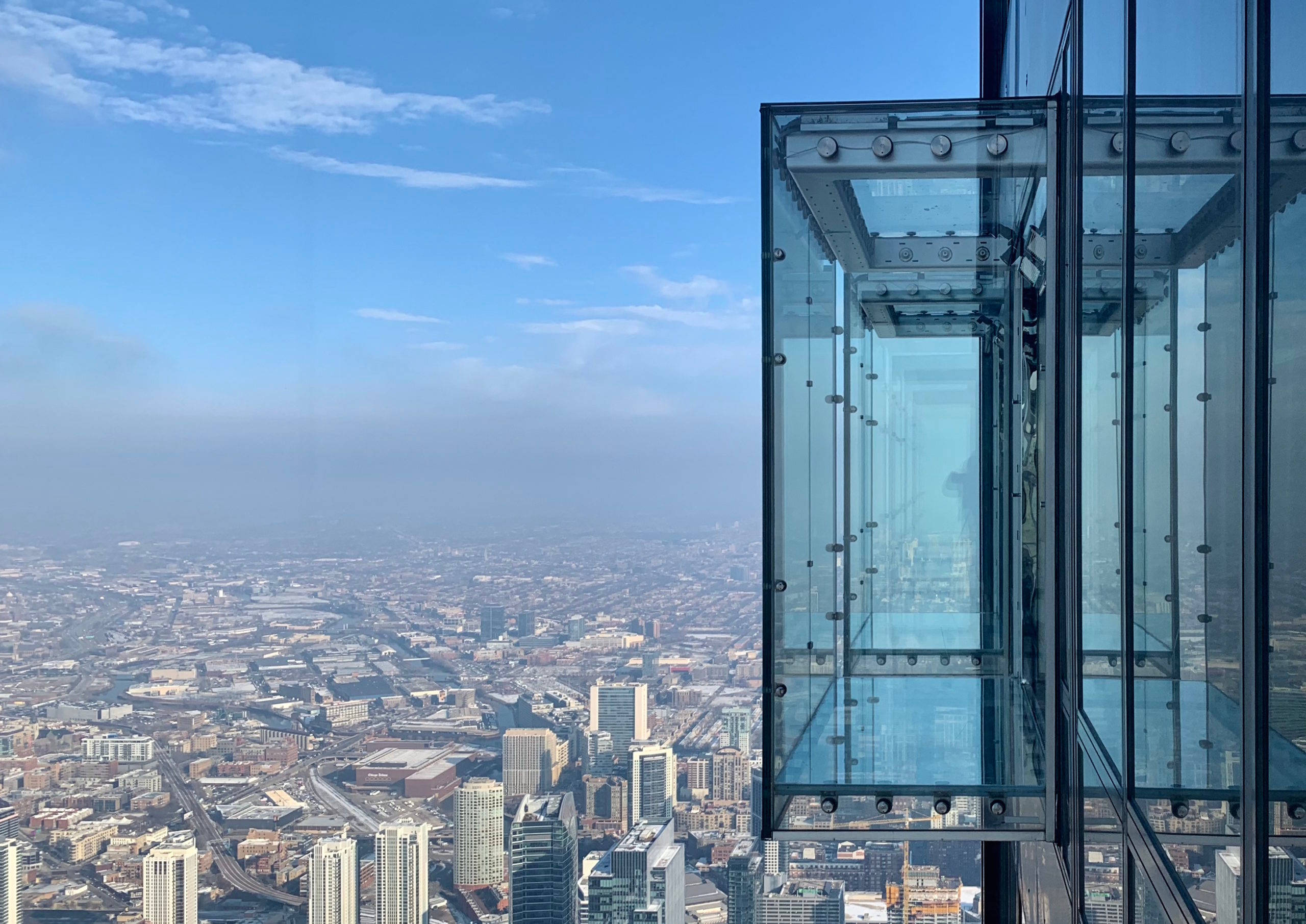 tower 桌布 壁紙 — 玻璃升降機在一片晴朗藍天和縷縷白雲下，攀升至廣闊城市景觀之上。