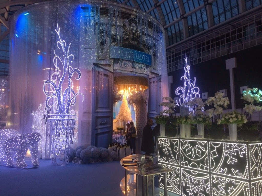 Ice Hotel 桌布 壁紙 — 玻璃屋頂下，宏偉的冰飯店入口裝飾著發光的藍色和白色燈光、雪花和花卉佈置。