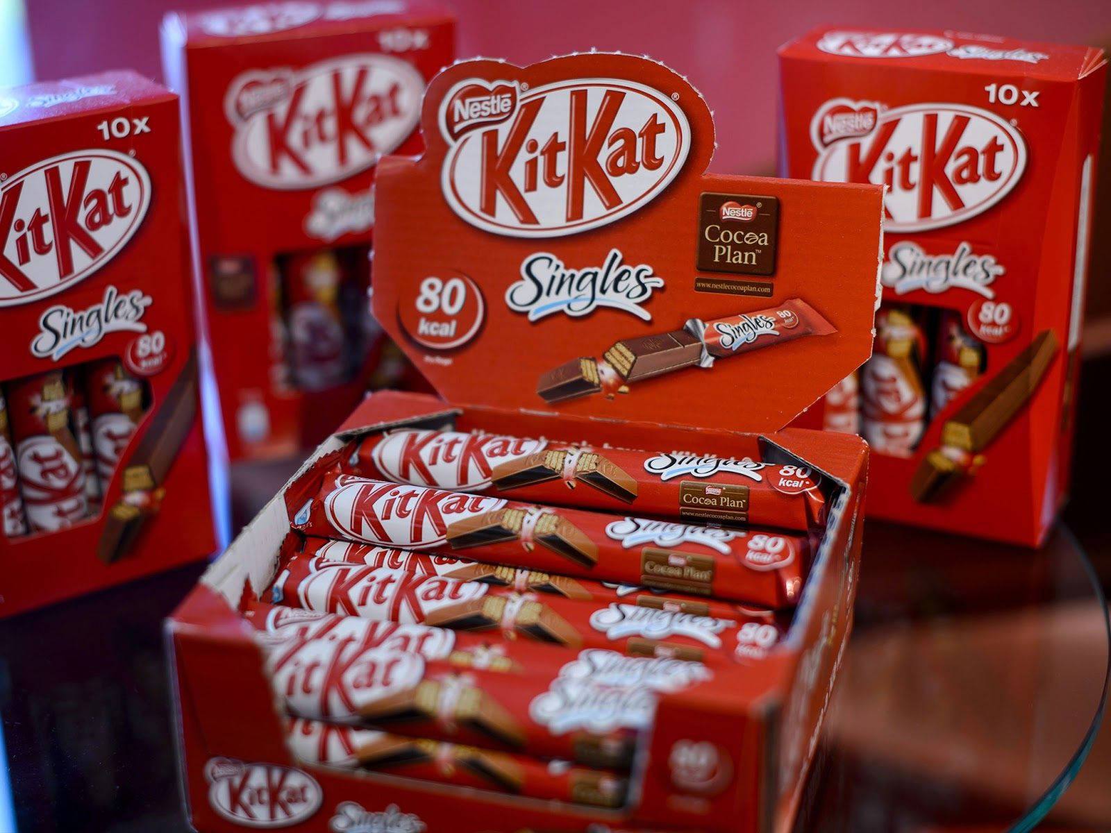Chocolate 桌布 壁紙 — 玻璃表面上展示的紅色KitKat Singles盒裝，內有獨立包裝的巧克力條。