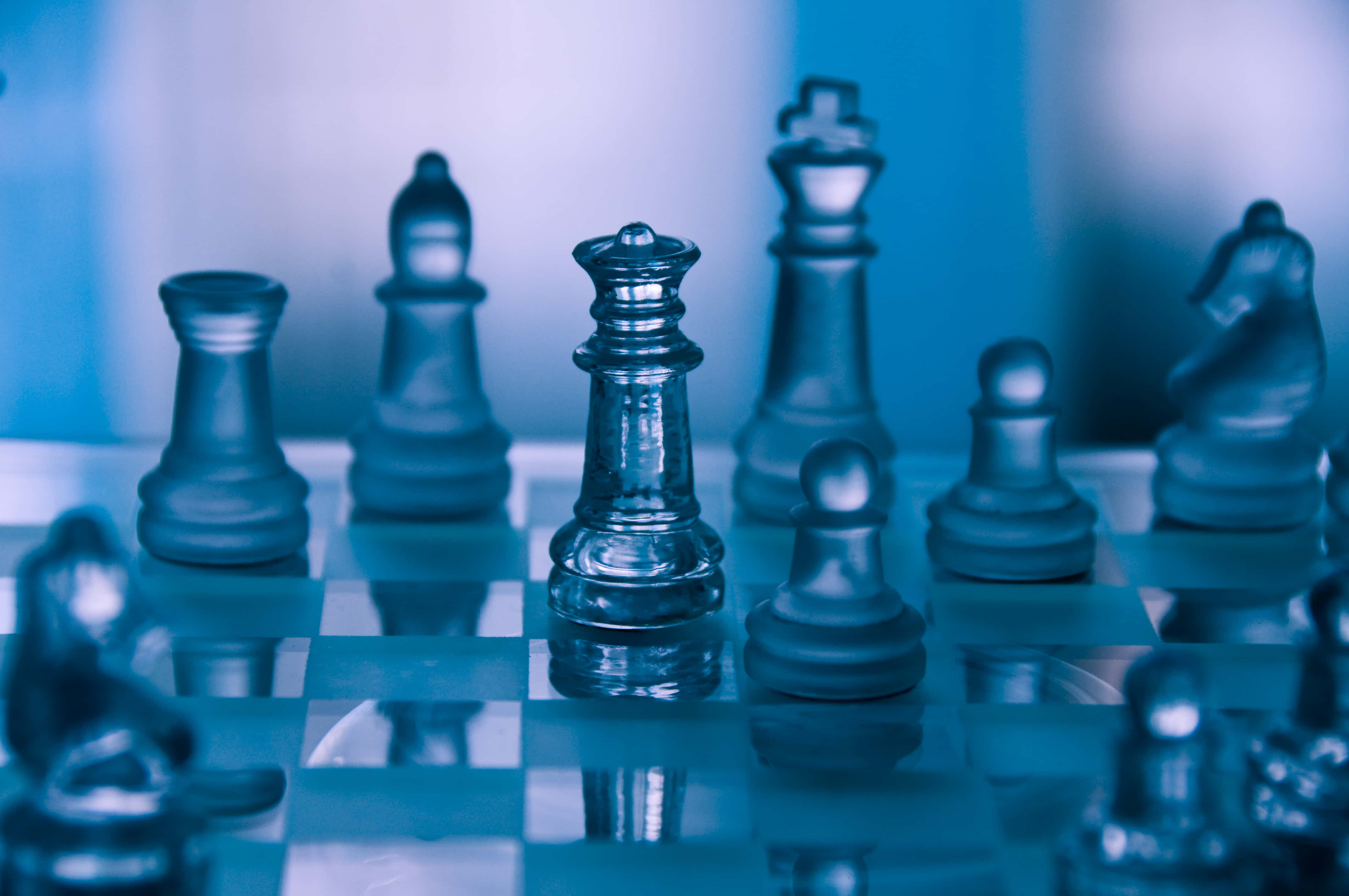 Chessboard 桌布 壁紙 — 玻璃西洋棋棋子清晰聚焦在反光棋盤上，背景模糊，冷藍色燈光下。