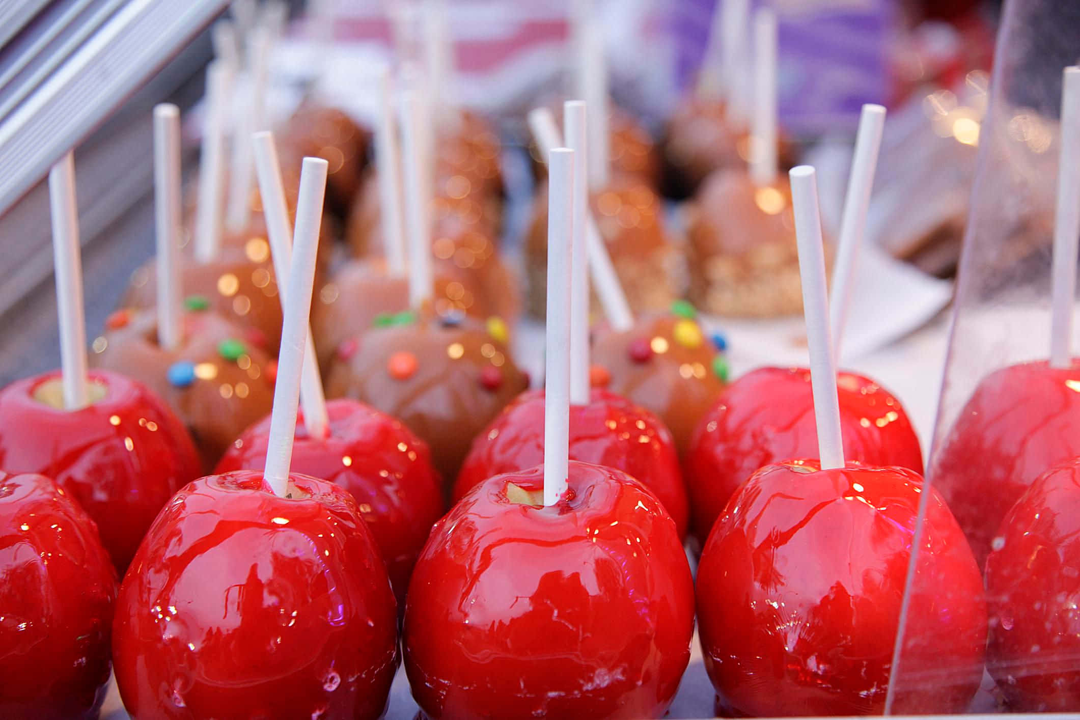 Candy Apples 桌布 壁紙 — 玻璃陳列櫃中展示的一排排光滑的紅色和棕色糖果蘋果，上面有彩色糖粒和白色棒。