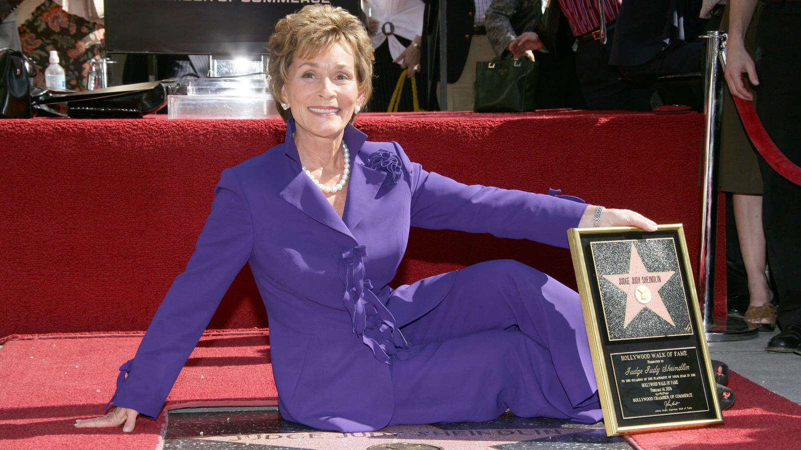 Judge Judy 桌布 壁紙 — 珍·芳達穿著紫色西裝，自豪地微笑，坐在紅地毯上，旁邊是她的好萊塢星光大道星形牌匾。