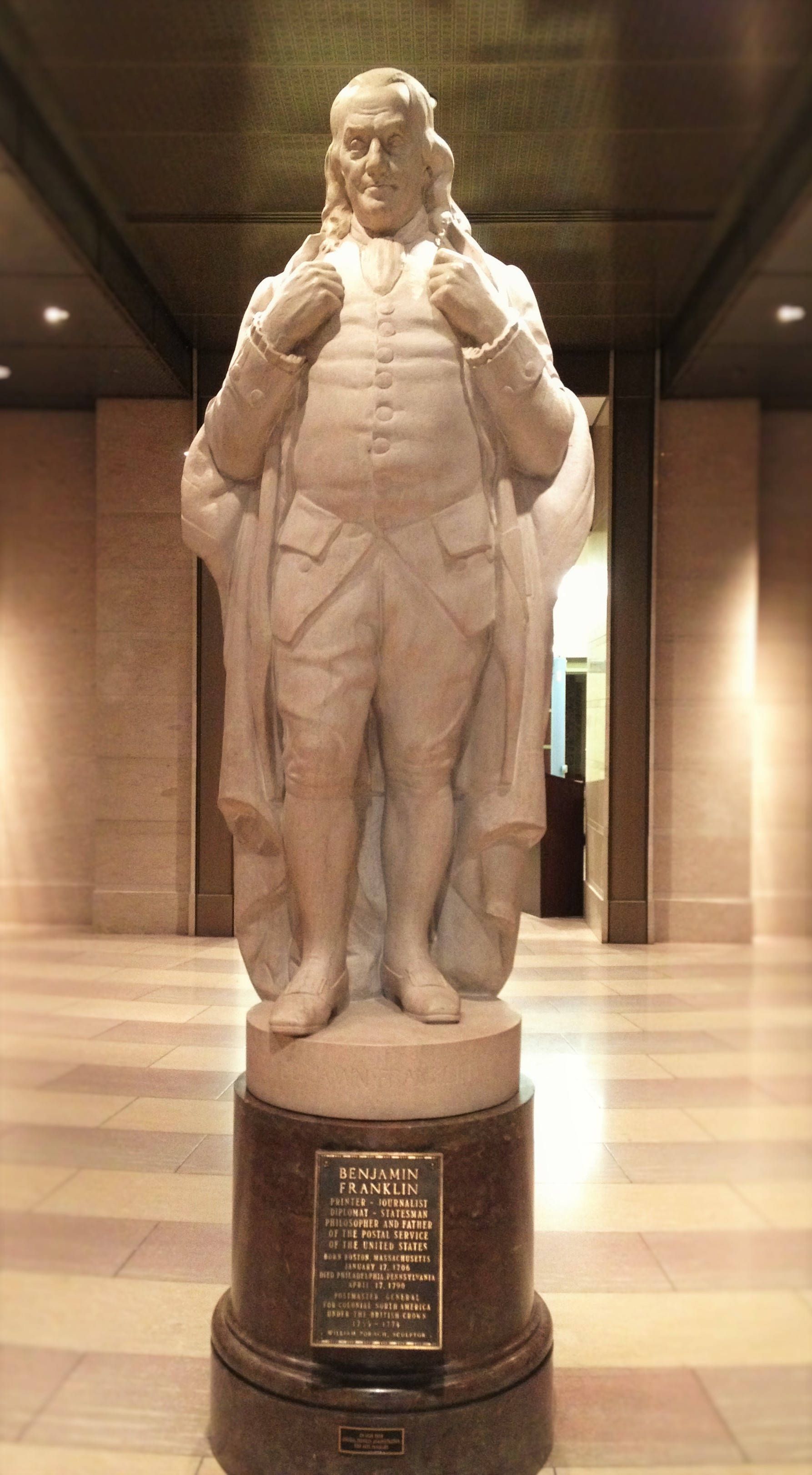 Franklin 桌布 壁紙 — 班傑明·富蘭克林的大理石雕像自豪地矗立在一個宏偉、燈光溫暖的博物館走廊中的深色基座上，走廊鋪有瓷磚地板和高大的柱子。