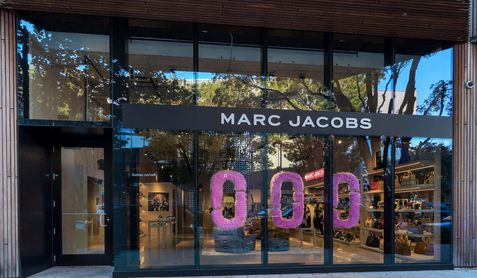 馬克·雅可布 桌布 壁紙 — 現代 Marc Jacobs 店面外牆，設有大型玻璃窗，反射樹木並展示店內巨大的粉紅色泡泡字母。