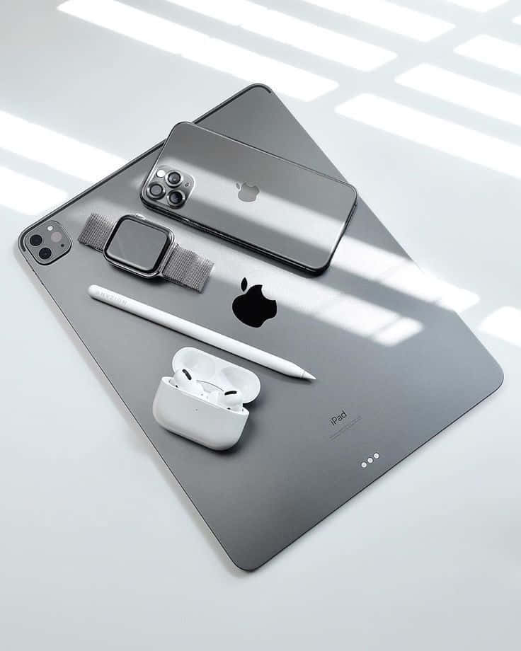 iPhone 12 桌布 壁紙 — 現代Apple裝置包括iPad、iPhone、Apple Watch和AirPods，排列在時尚的灰色表面上，明亮的窗戶光線投射出幾何陰影。